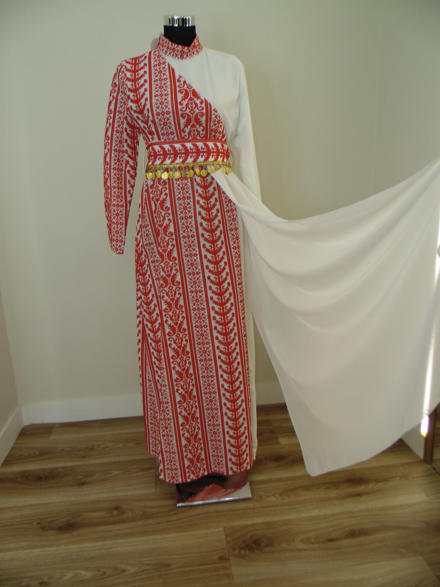 Traditional embroidered garment on a white stand with wooden floor background