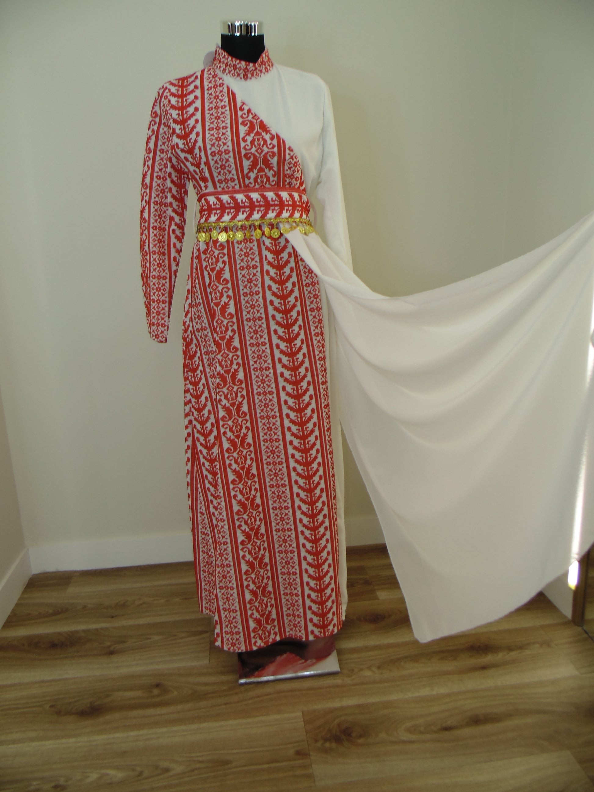 Traditional embroidered garment on a white stand with wooden floor background