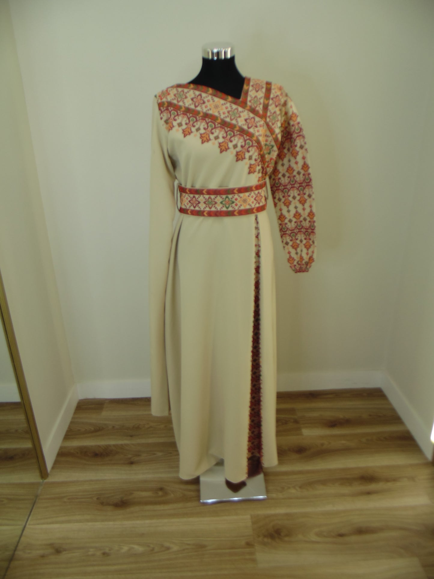 Beige dress with floral patterned trim on a mannequin against a wooden panel background