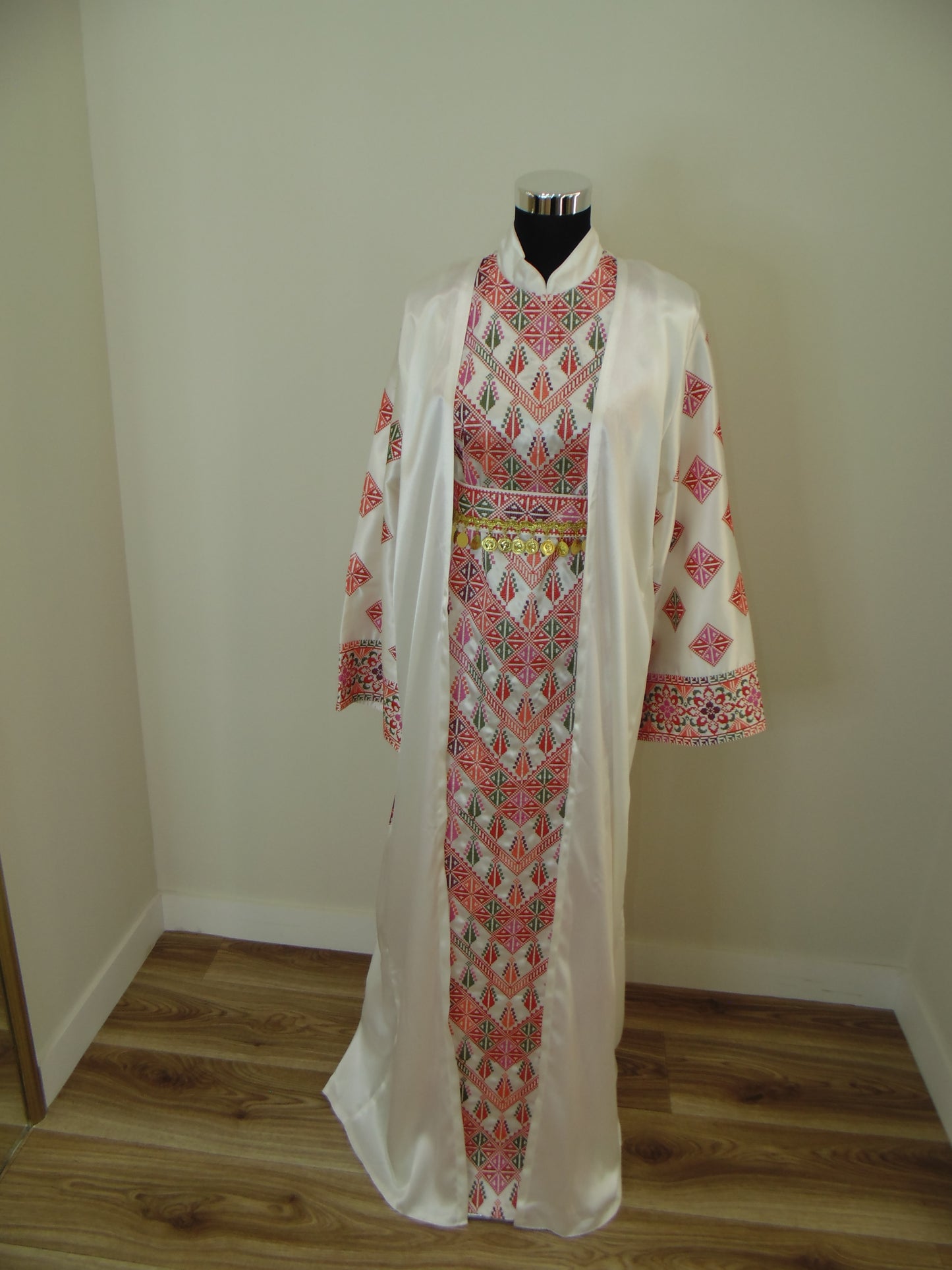 Traditional embroidered garment on a wooden stand against a white wall