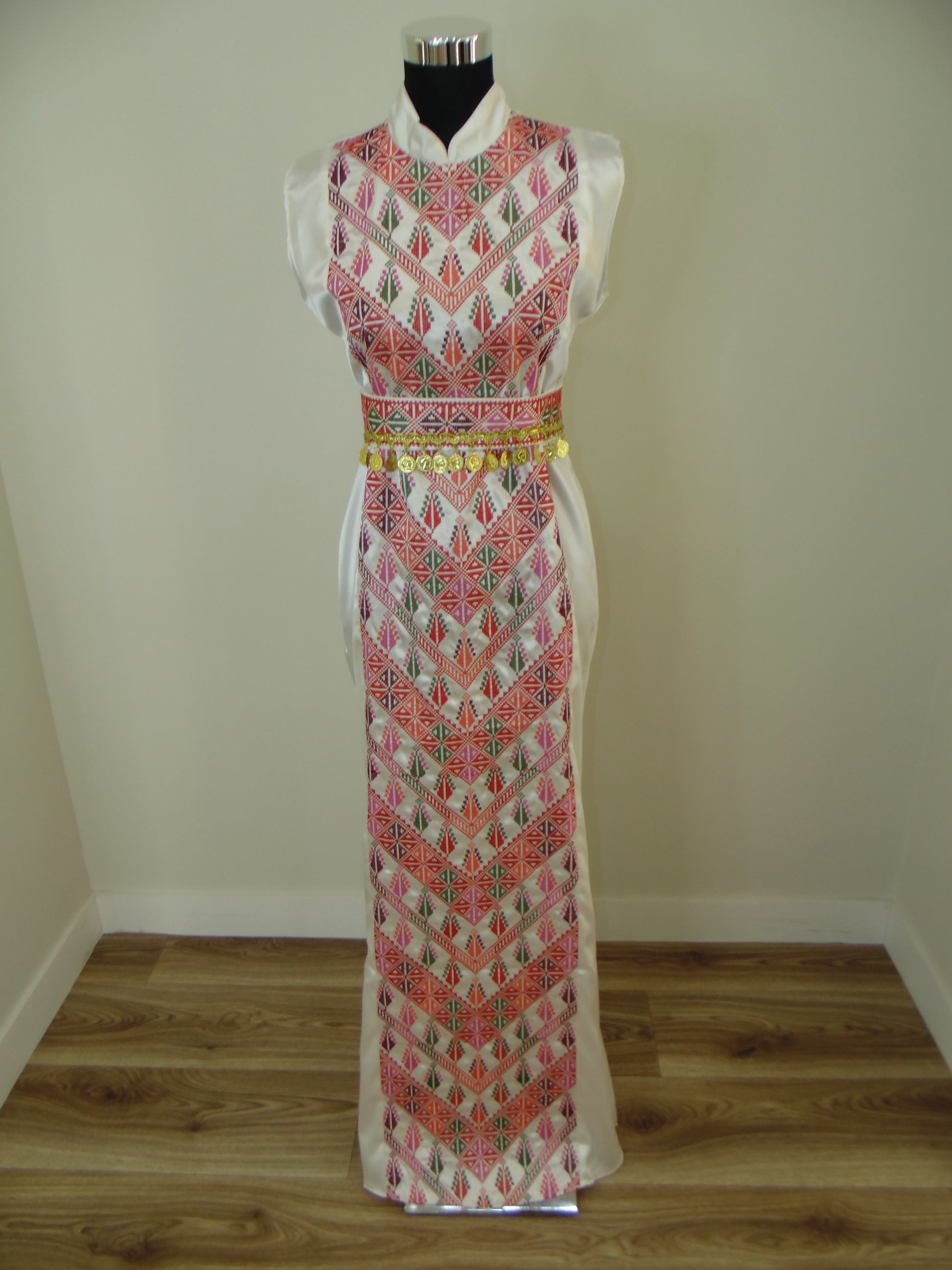 Traditional dress with intricate patterns on a mannequin against a plain wall.