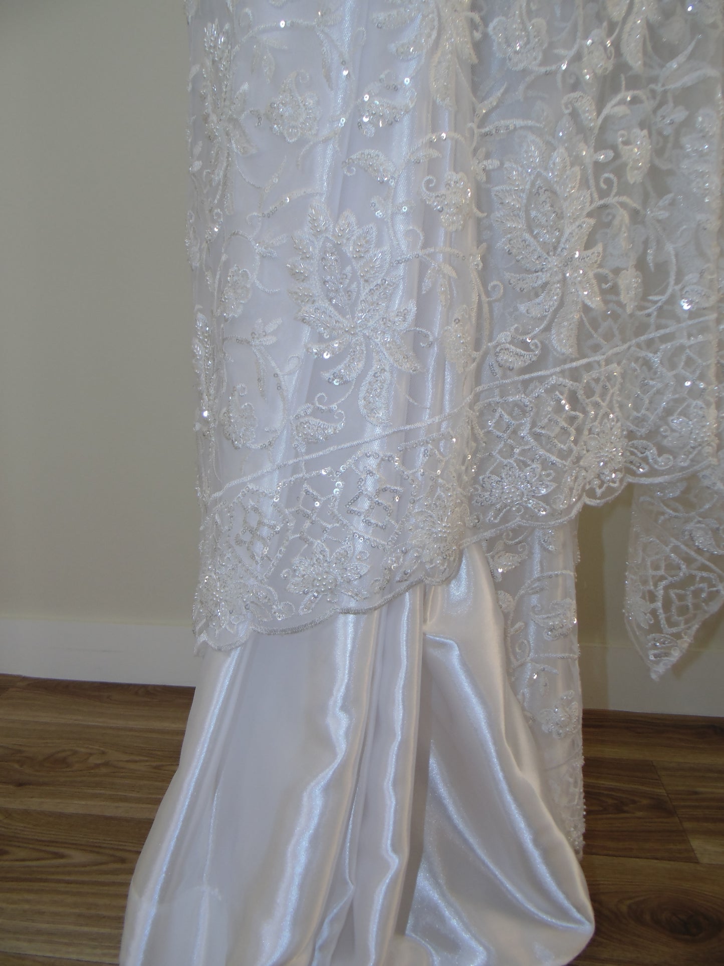 Close-up of a white lace wedding dress on a wooden surface.