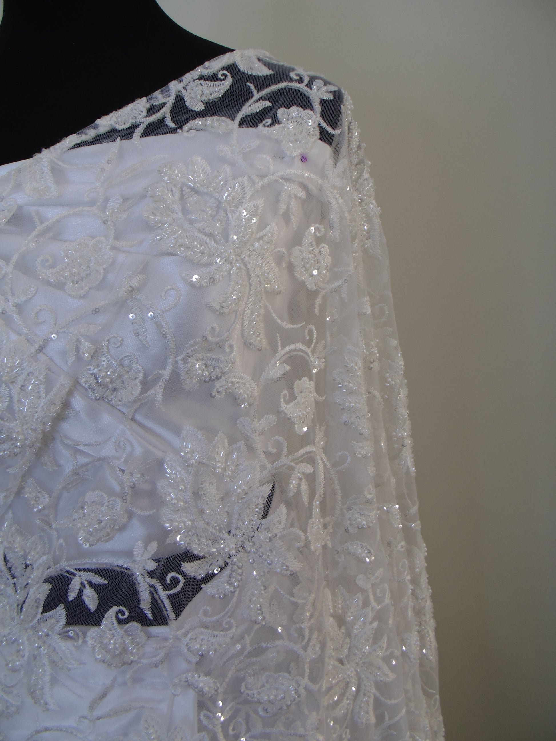 Close-up of a white lace fabric with black floral patterns on a plain background