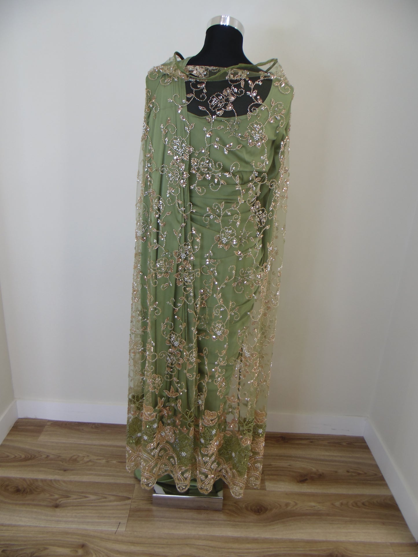 Green embroidered saree with cardigan on a mannequin against a white wall.