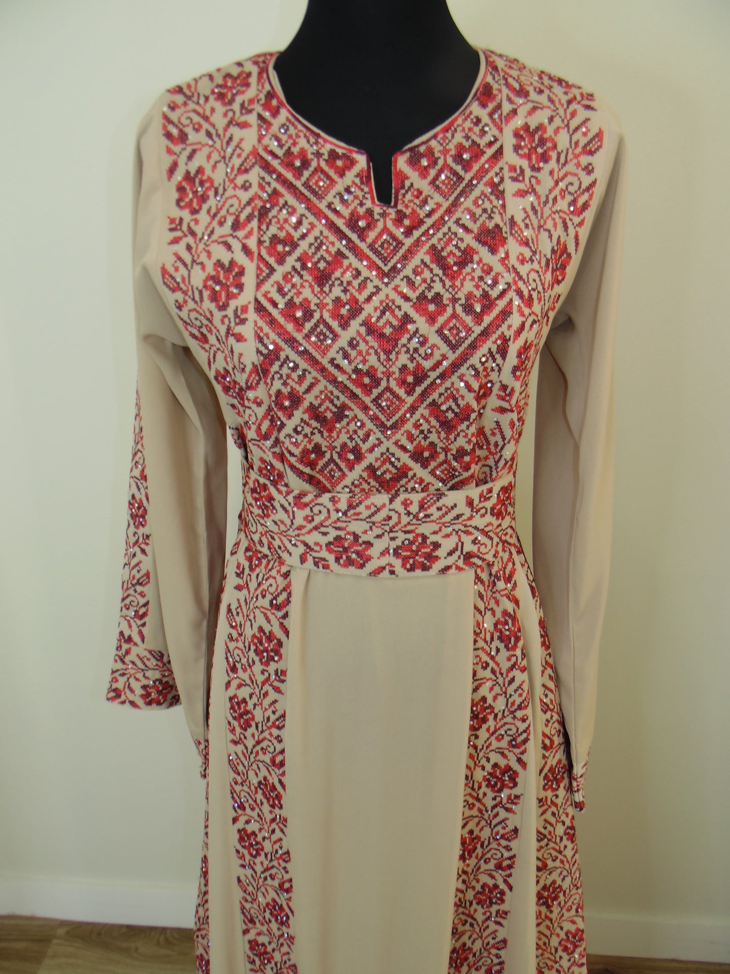 Red and white patterned palestinian Thobe on a mannequin against a plain background