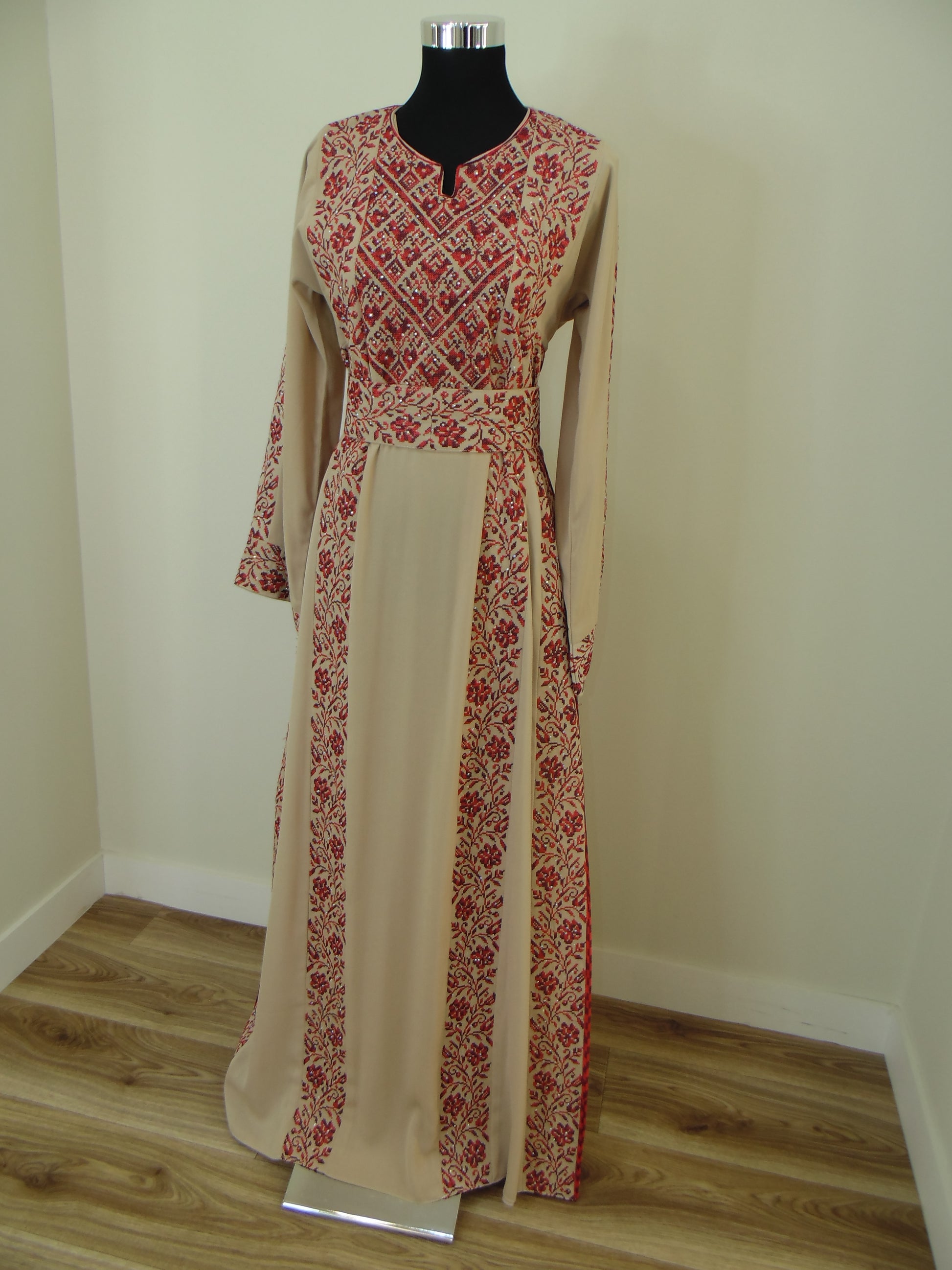 Traditional dress with red patterns on a wooden hanger against a white wall.