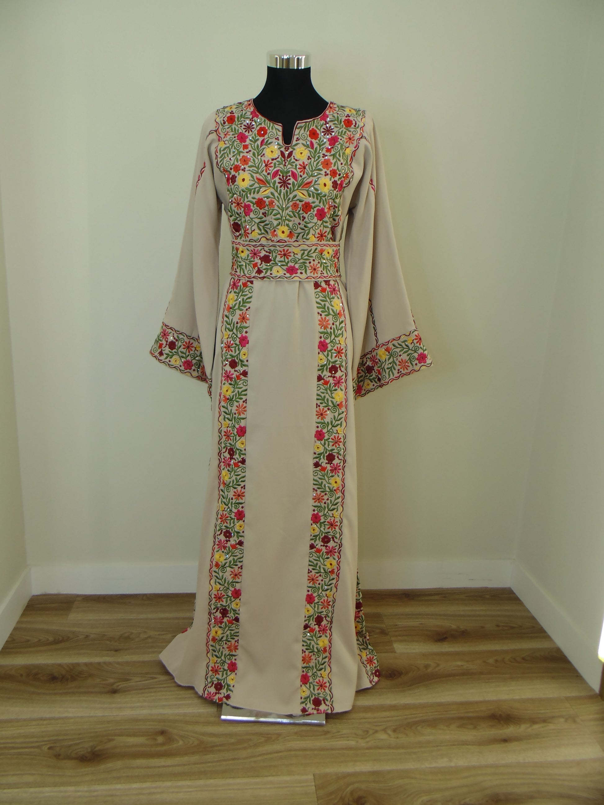 Palestinian Thobe with floral pattern hanging on a wooden rod against a white wall.