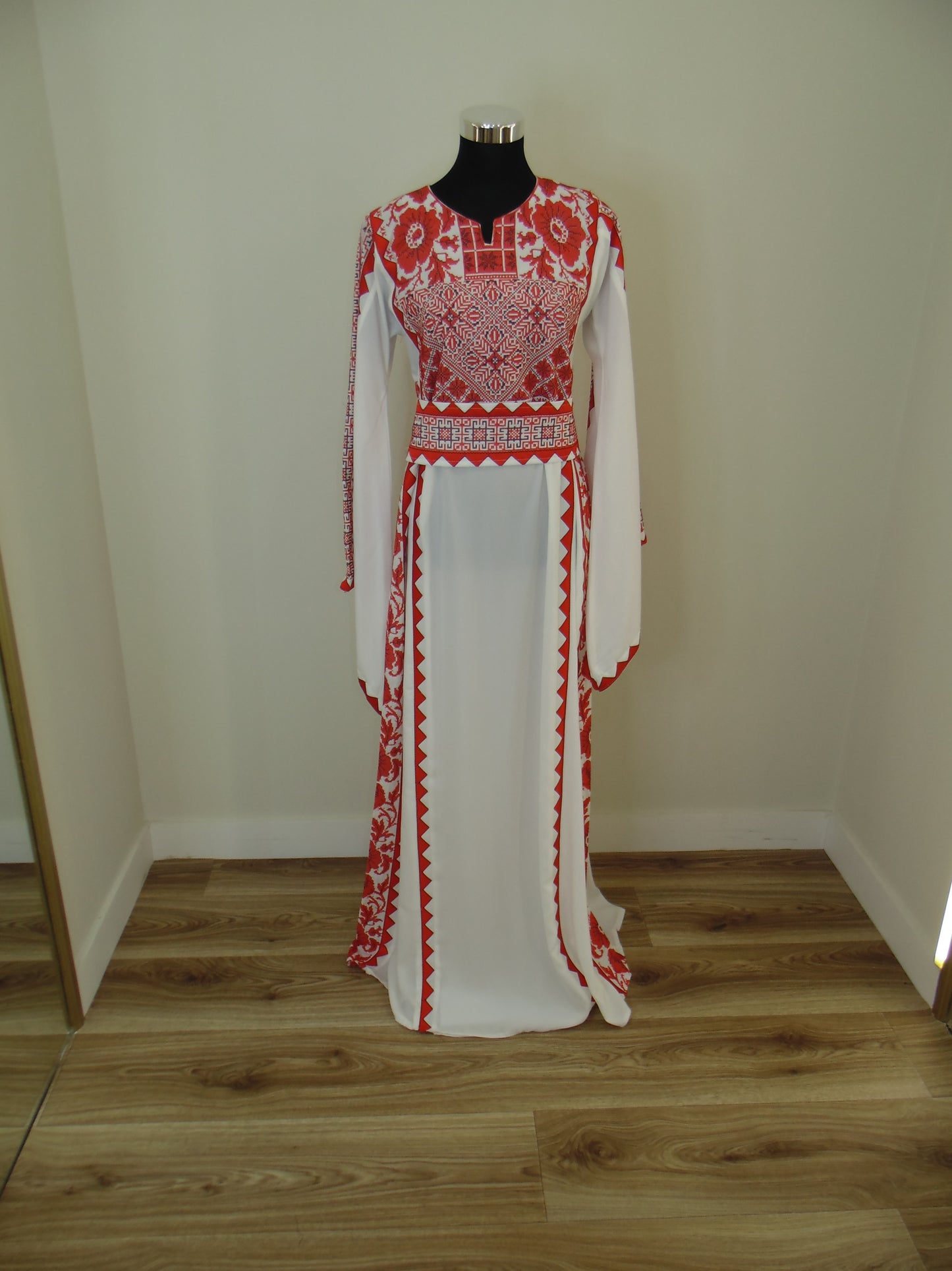 Traditional embroidered garment on a mannequin against a wooden wall.