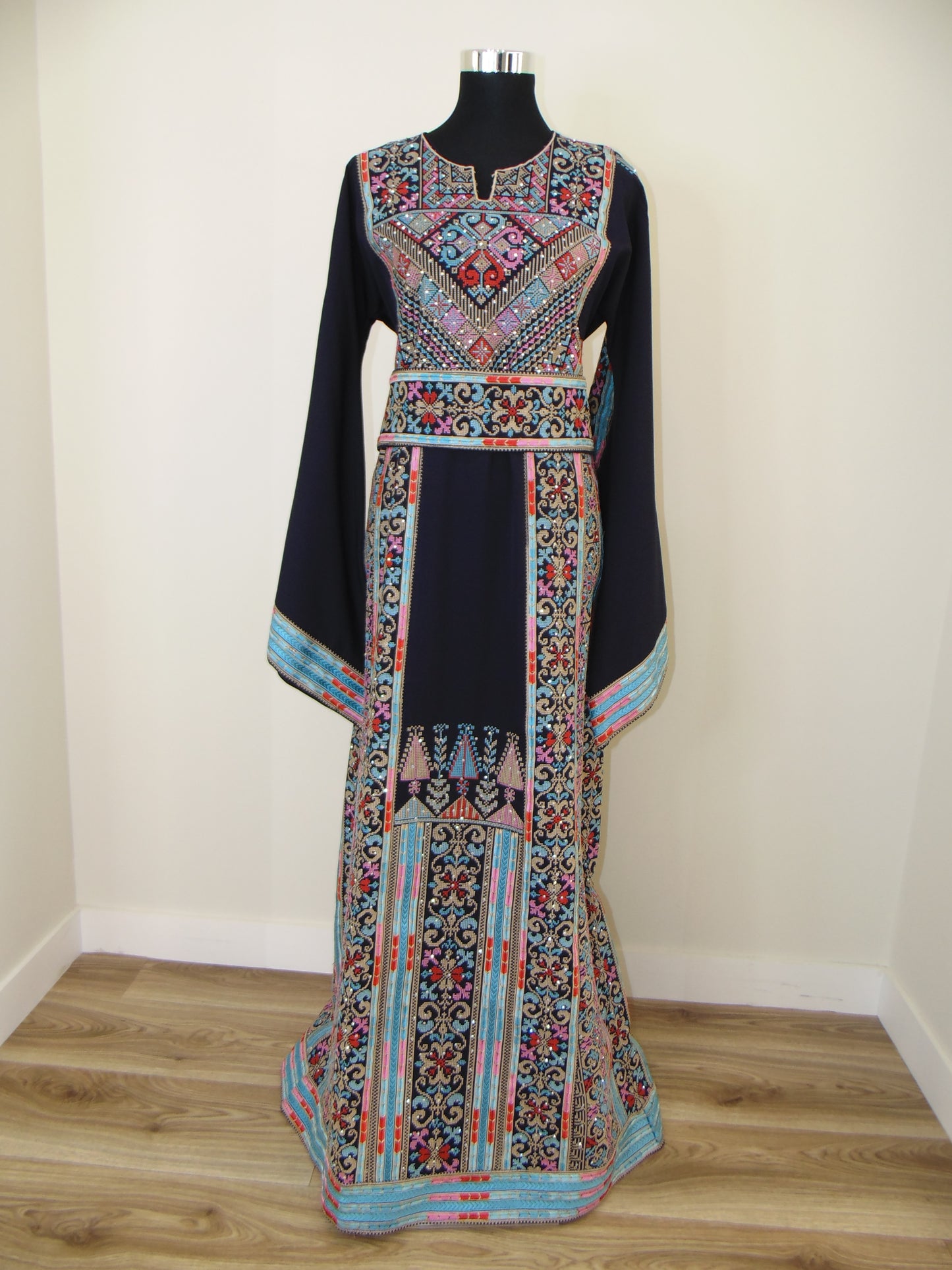 Colorful embroidered Palestinian Thobe on a white surface with wooden floor background