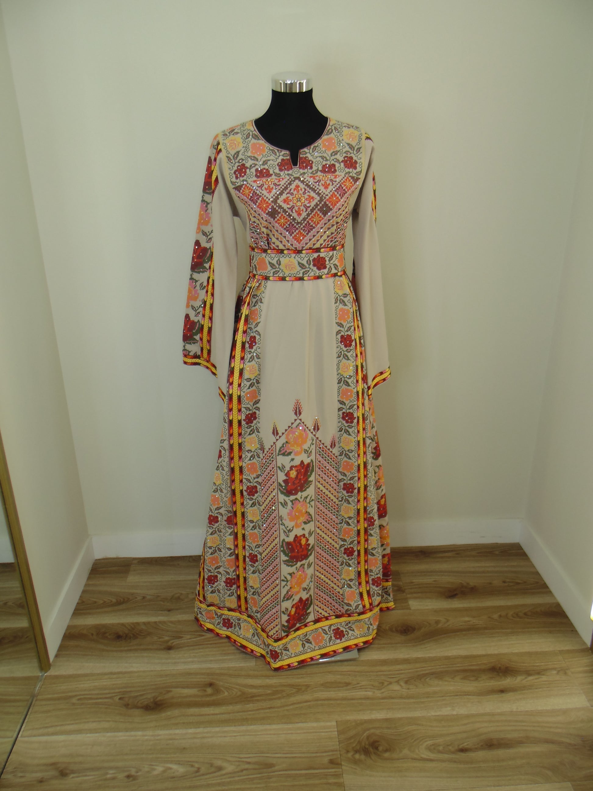 Traditional embroidered palestinian Thobe on a mannequin against a wooden wall.