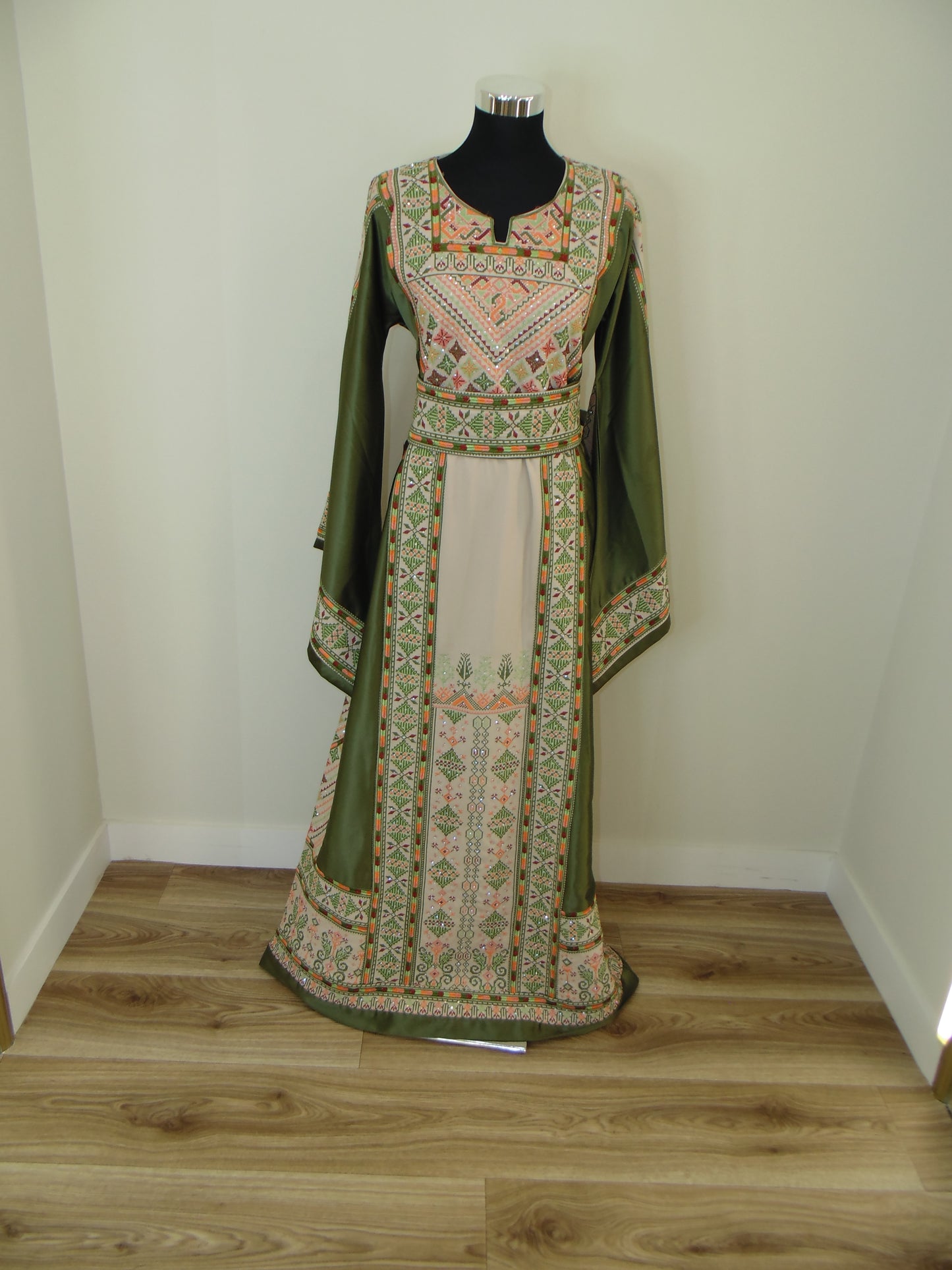 Traditional embroidered garment on a wooden stand against a white wall.