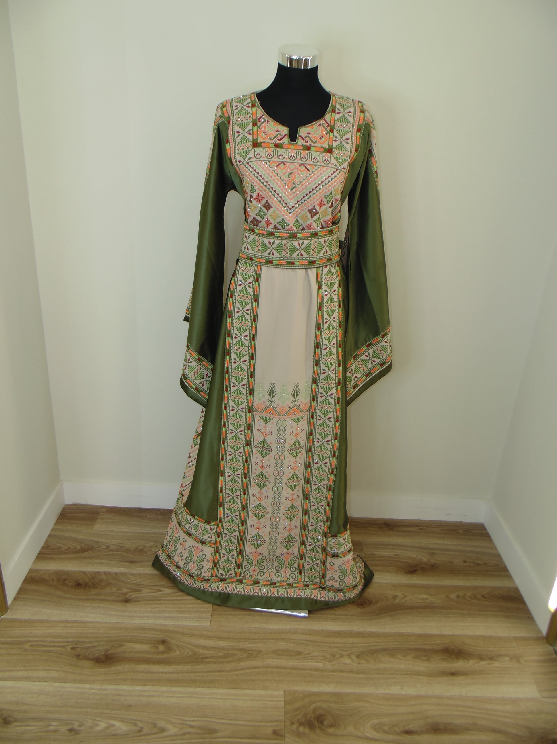 Traditional embroidered garment on a wooden stand against a white wall.