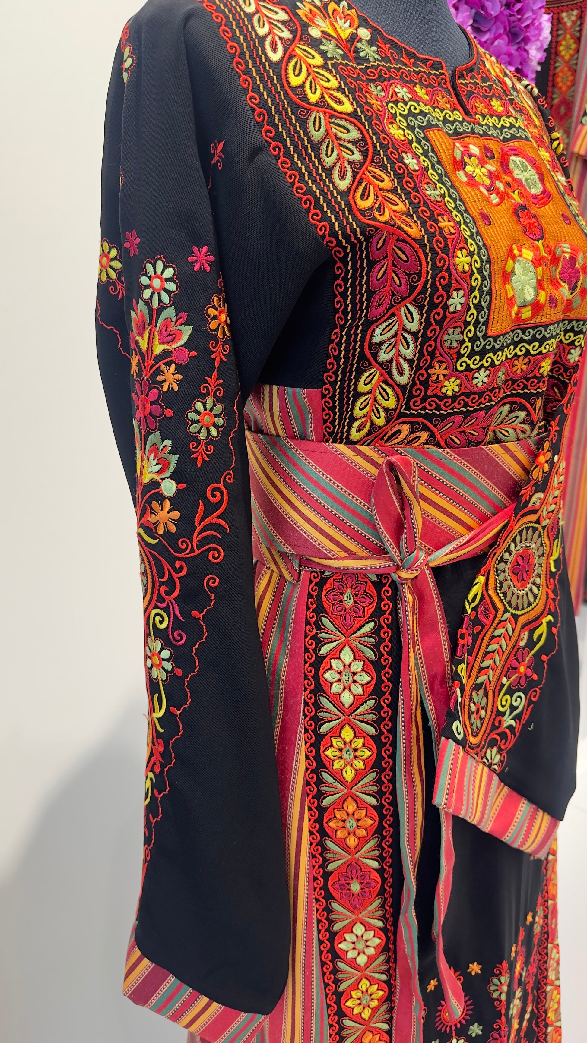 Colorful embroidered Thobewith a belt on a plain background