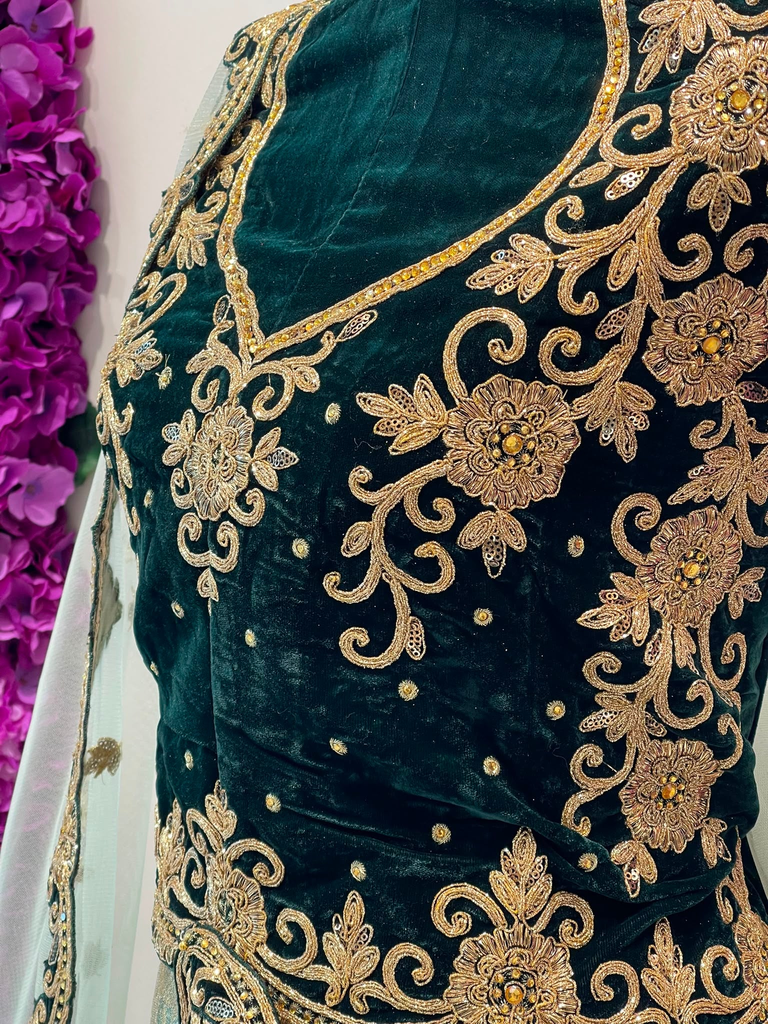 Close-up of a dark green velvet embroidered blouse with intricate gold floral and scrollwork embroidery, featuring a V-neckline and decorative beadwork.