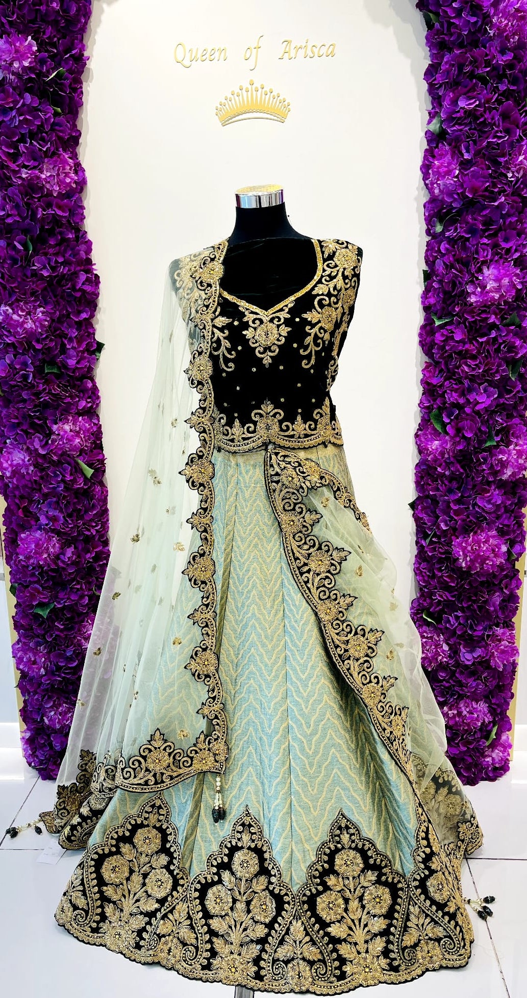 A traditional Indian lehenga choli dress . The outfit features a green embroidered choli with gold detailing, a light mint green skirt with gold embroidery, and a sheer mint green dupatta.