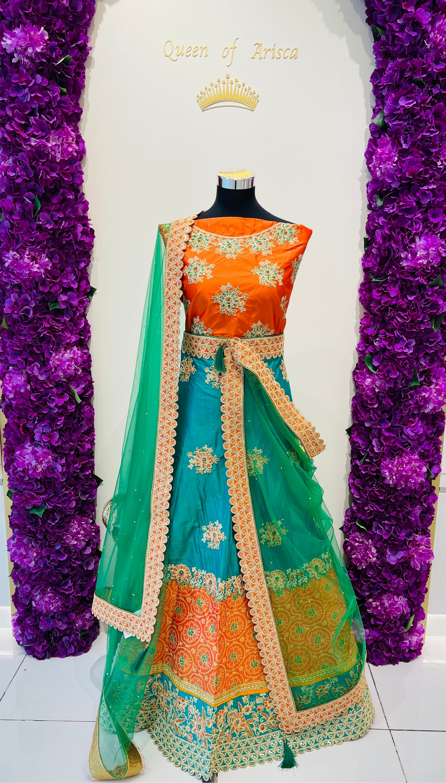 A vibrant orange and teal green traditional Indian lehenga set with intricate gold embroidery.