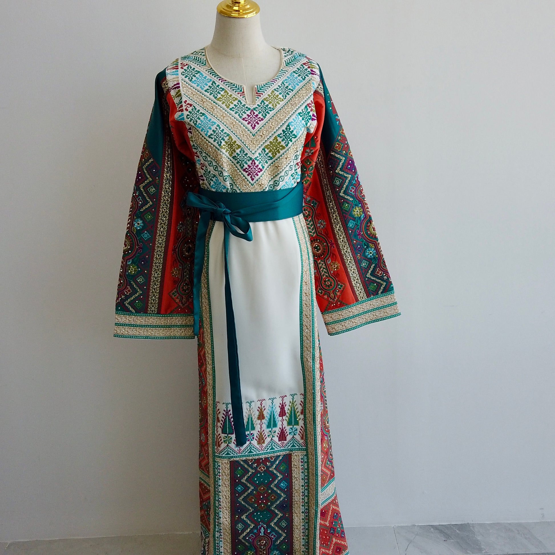 Detail shot of Palestinian Tatreez with teal, magenta, and olive accents on white