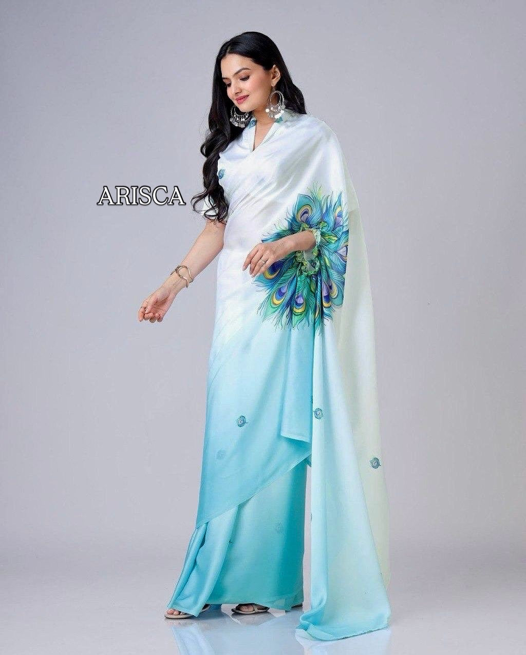 Woman wearing a white and blue saree with peacock design on a gray background