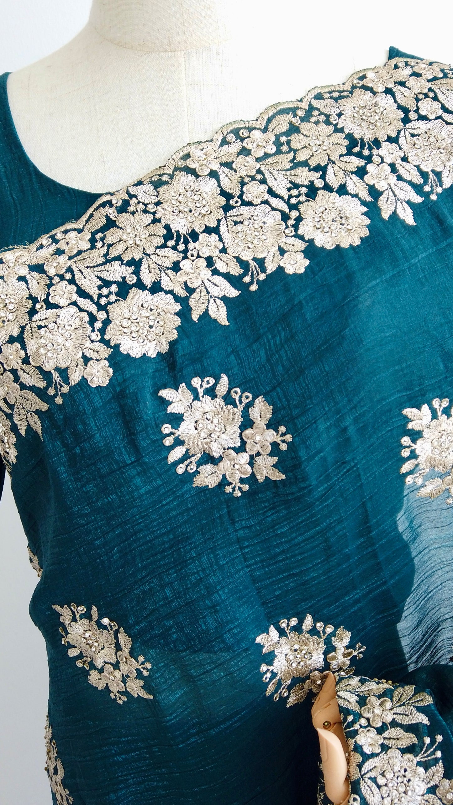 Close-up of intricate gold embroidery on teal green silk fabric.