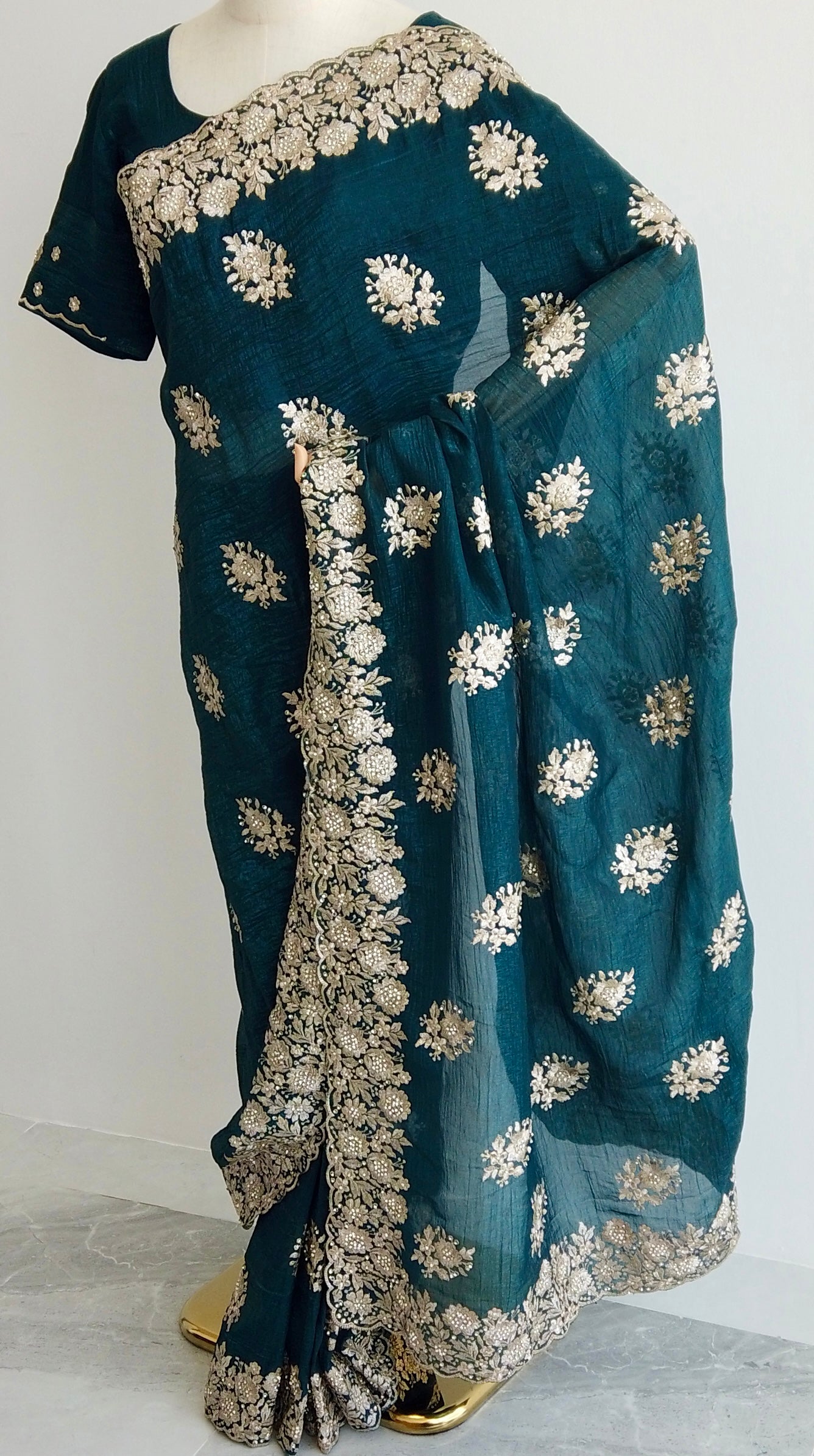 Teal green ready-to-wear saree with gold floral embroidery displayed on a mannequin