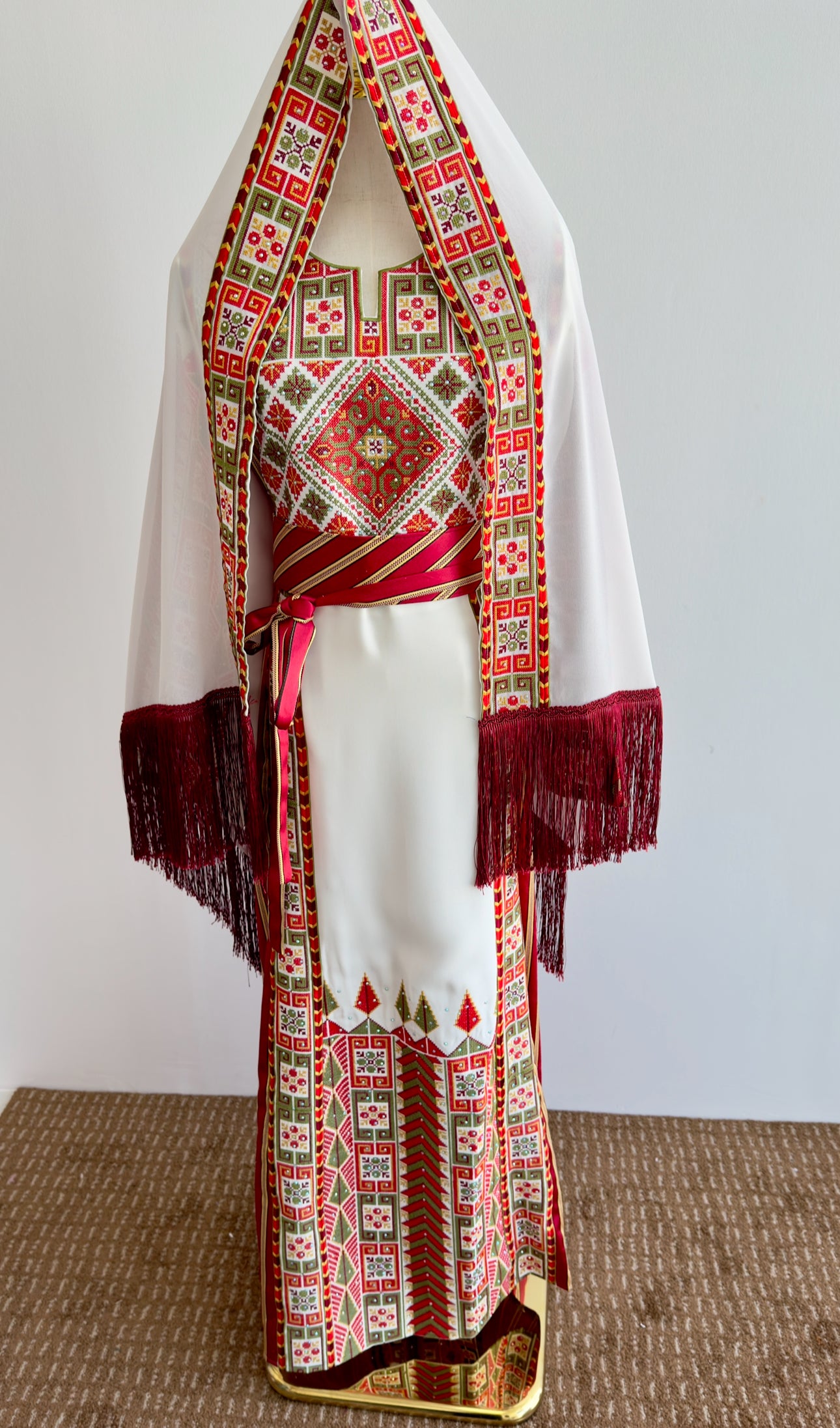 Front view of Palestinian thobe with intricate red, green, and gold embroidery on white fabric.