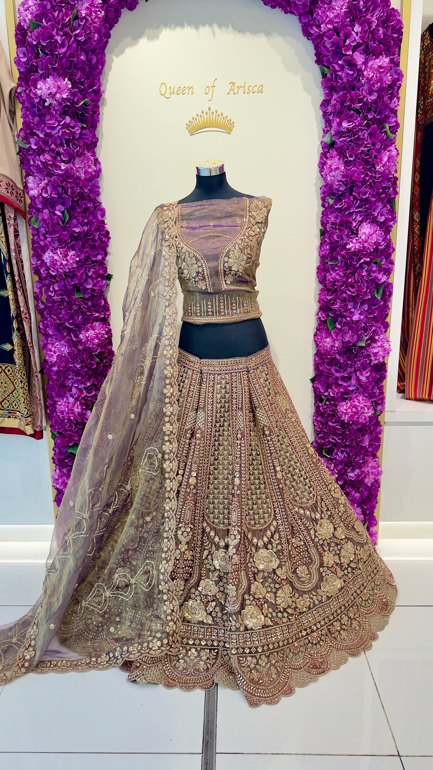 Delicate embroidered lehenga with a matching blouse on a mannequin against a decorative purple floral background.