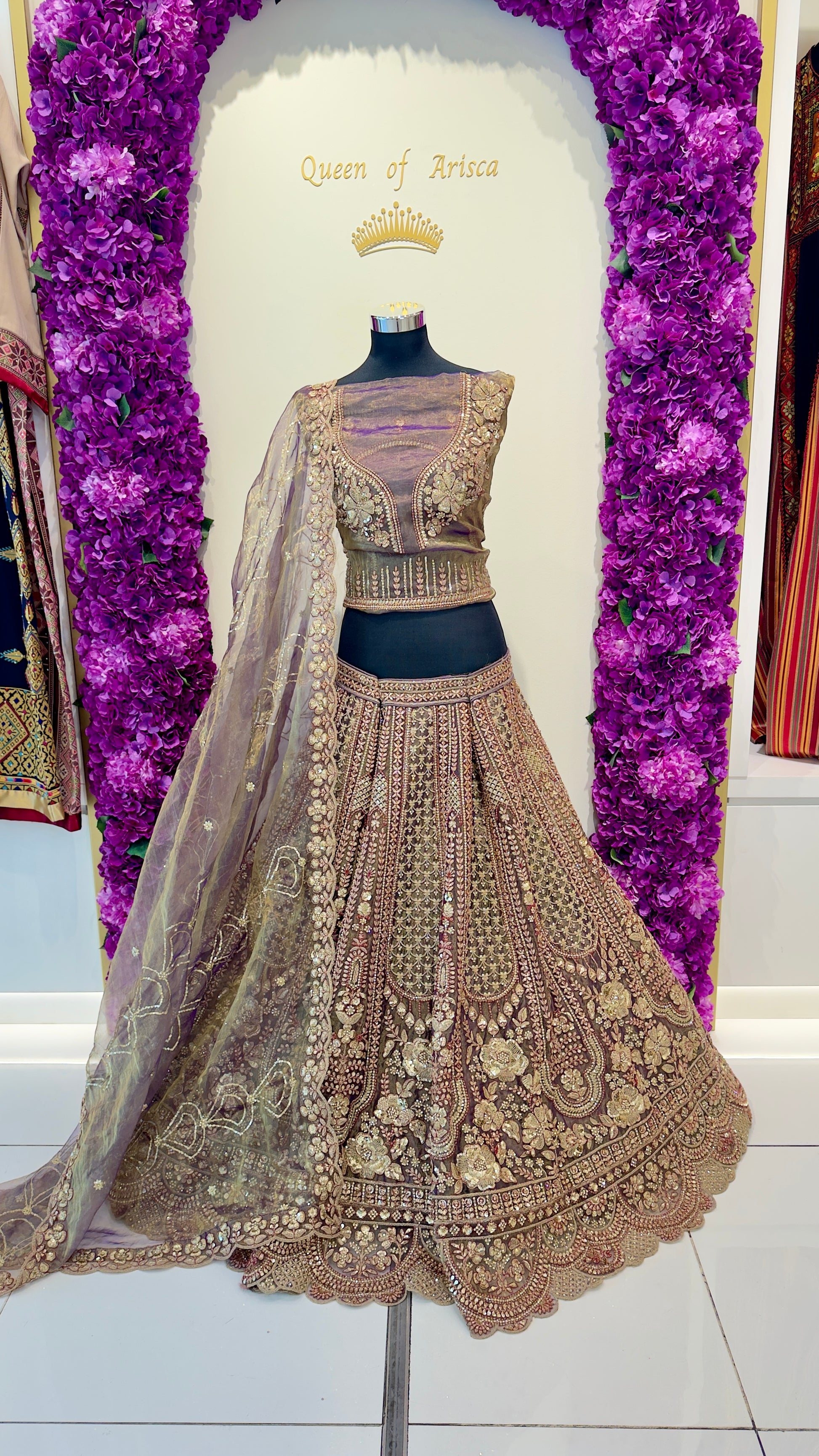 Delicate embroidered lehenga with a matching blouse on a mannequin against a decorative purple floral background.