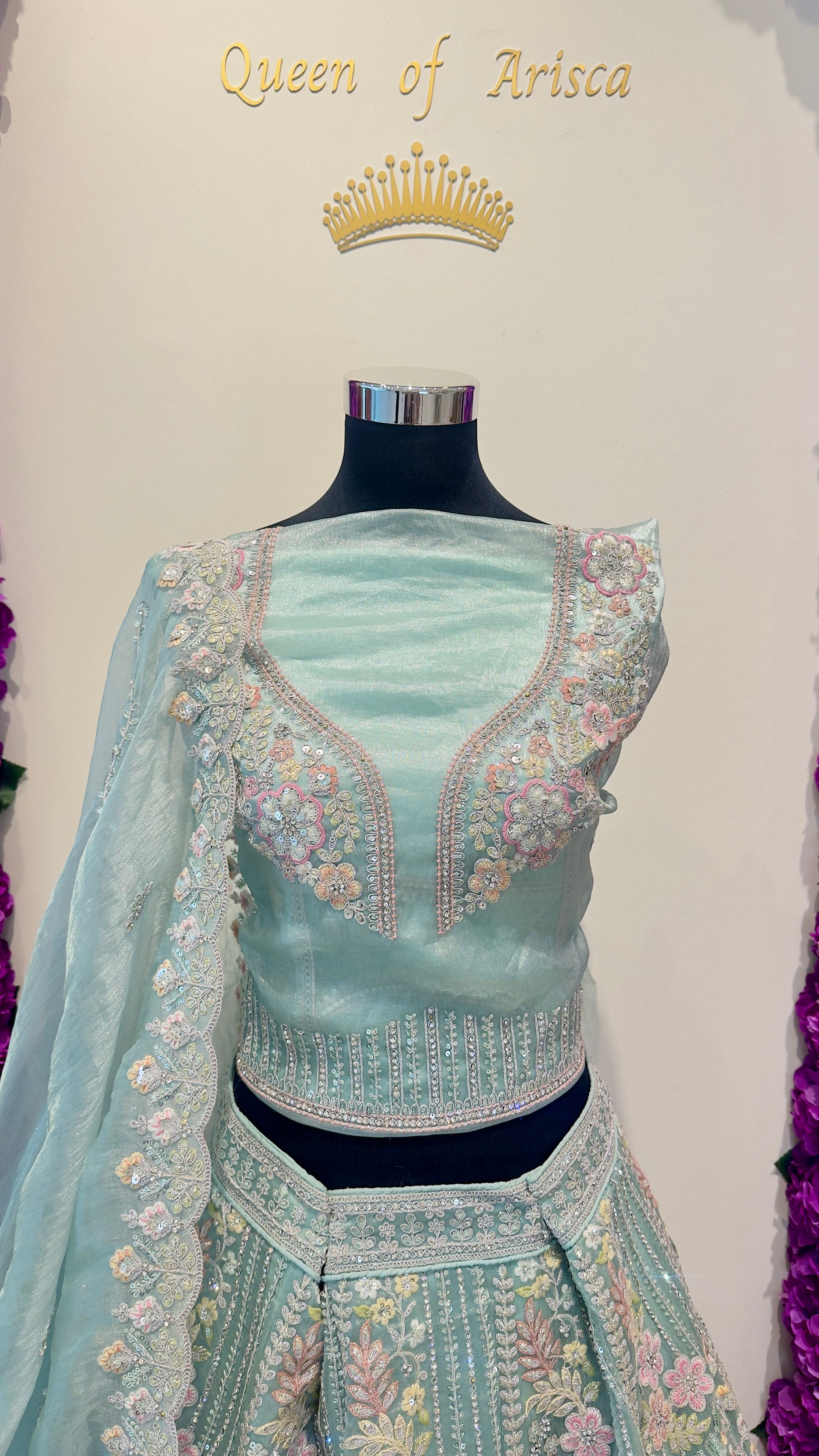 Light blue embroidered traditional outfit on a mannequin with 'Queen of Arisca' text above.
