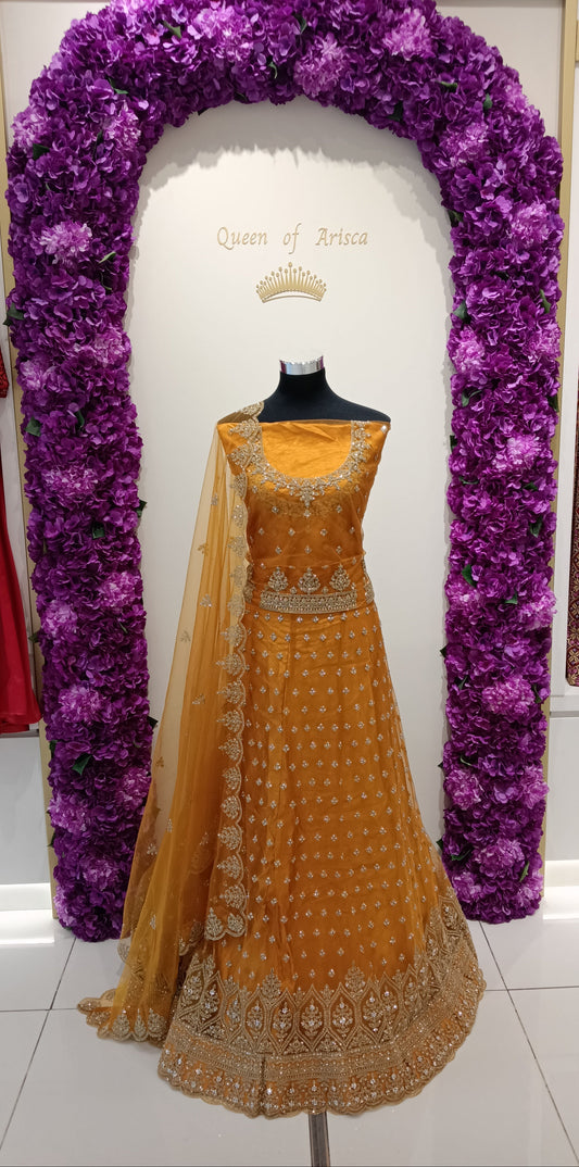rich mustard yellow lehenga with gold butti work and heavy embroidered borders. The warm tone is auspicious and perfect for special events in Qatar.