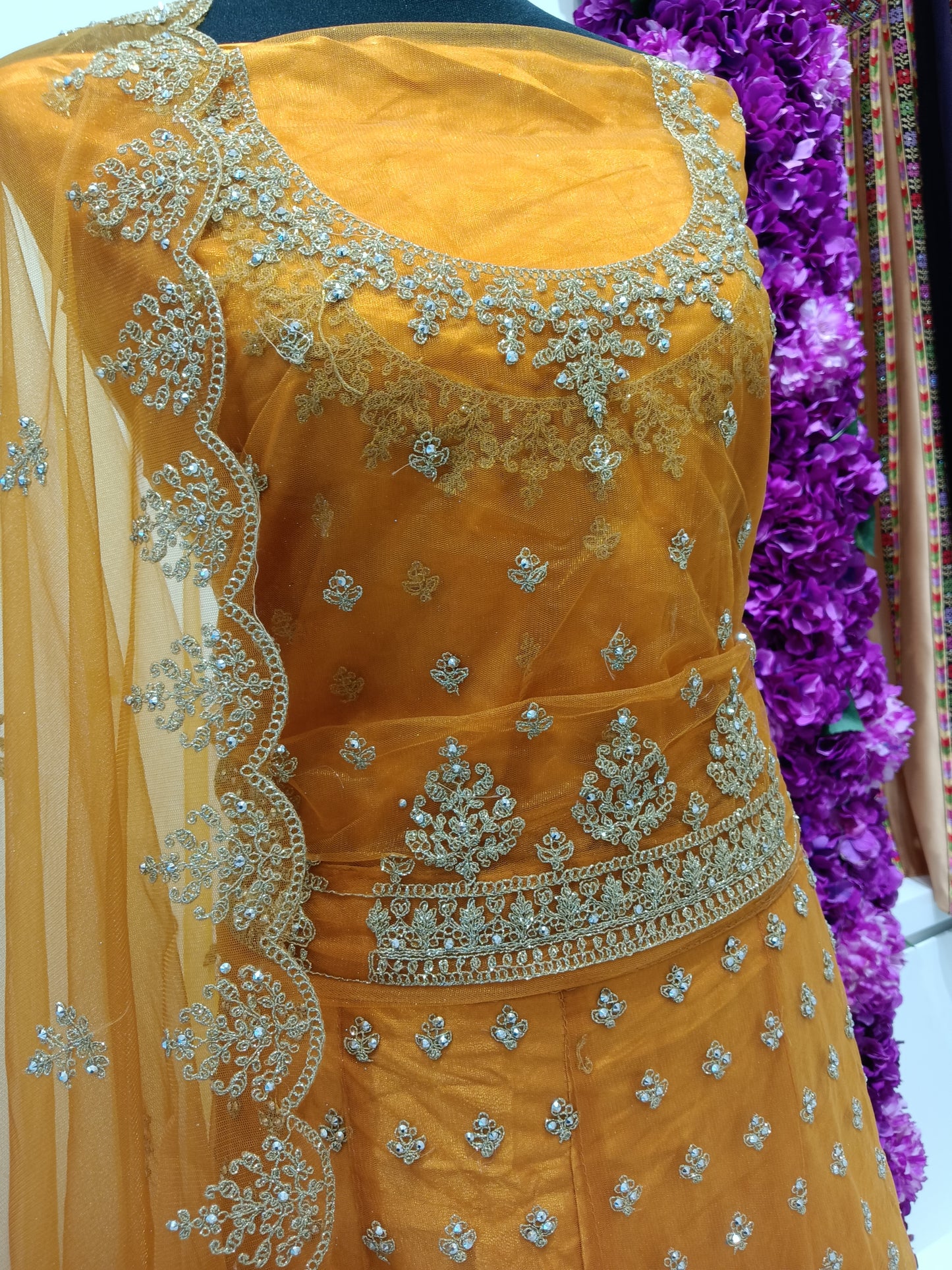 Lehenga Skirt: Net fabric with gold butti and ornate border work , Blouse: Heavily embroidered net with gold neckline detailing , Dupatta: Mustard net dupatta with scalloped embroidered border.