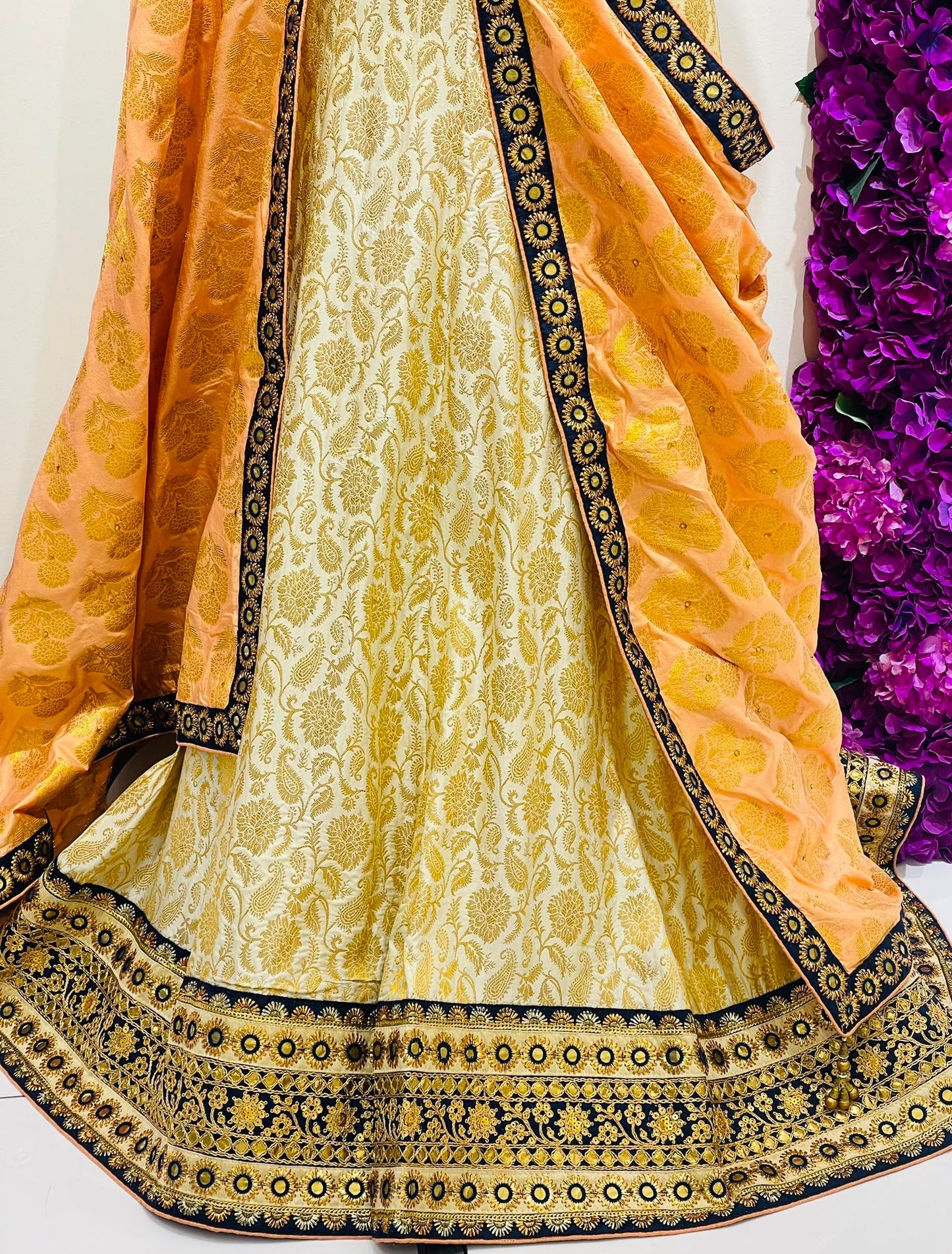 A traditional Indian ethnic outfit featuring a light yellow and gold brocade skirt with a wide navy blue and gold border, paired with a matching yellow dupatta draped over the shoulders.