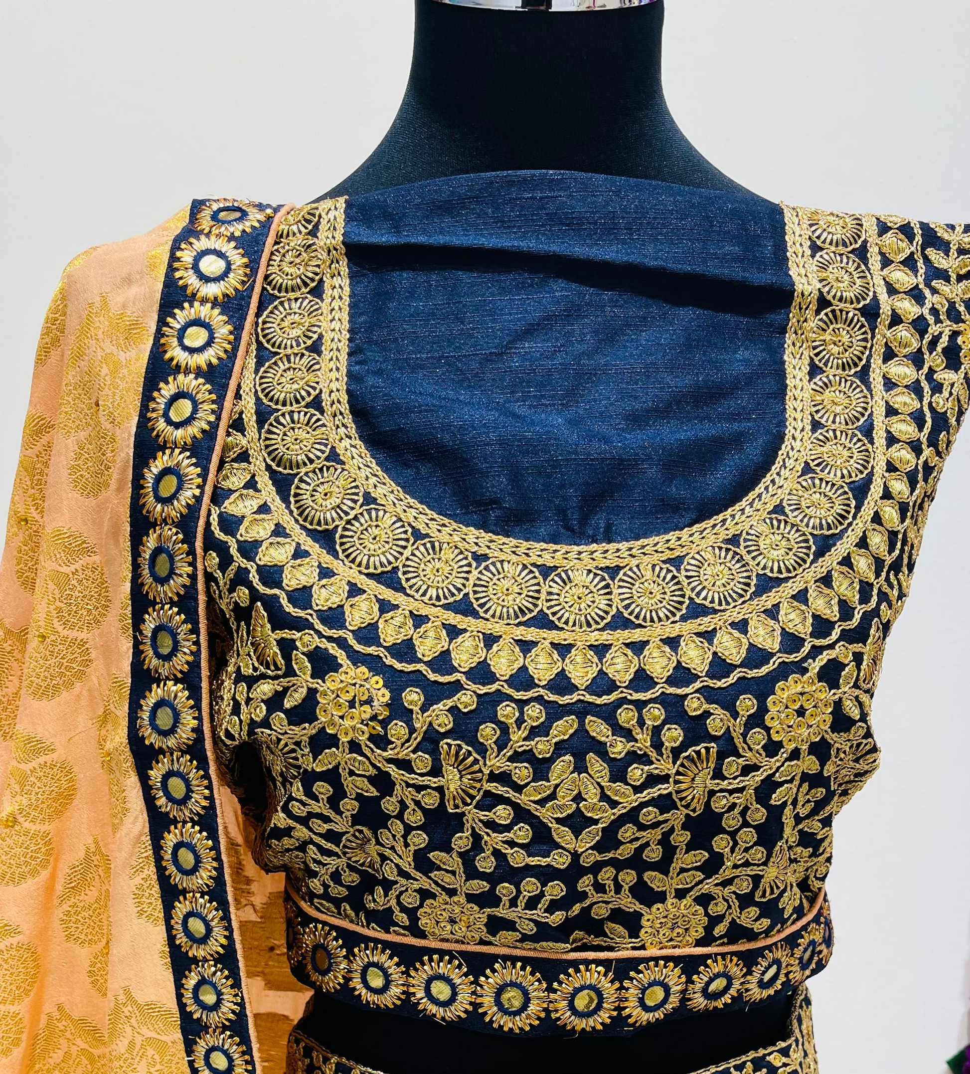 A traditional Indian lehenga, featuring a navy blue and gold embroidered blouse , and a peach-colored dupatta with gold borders.