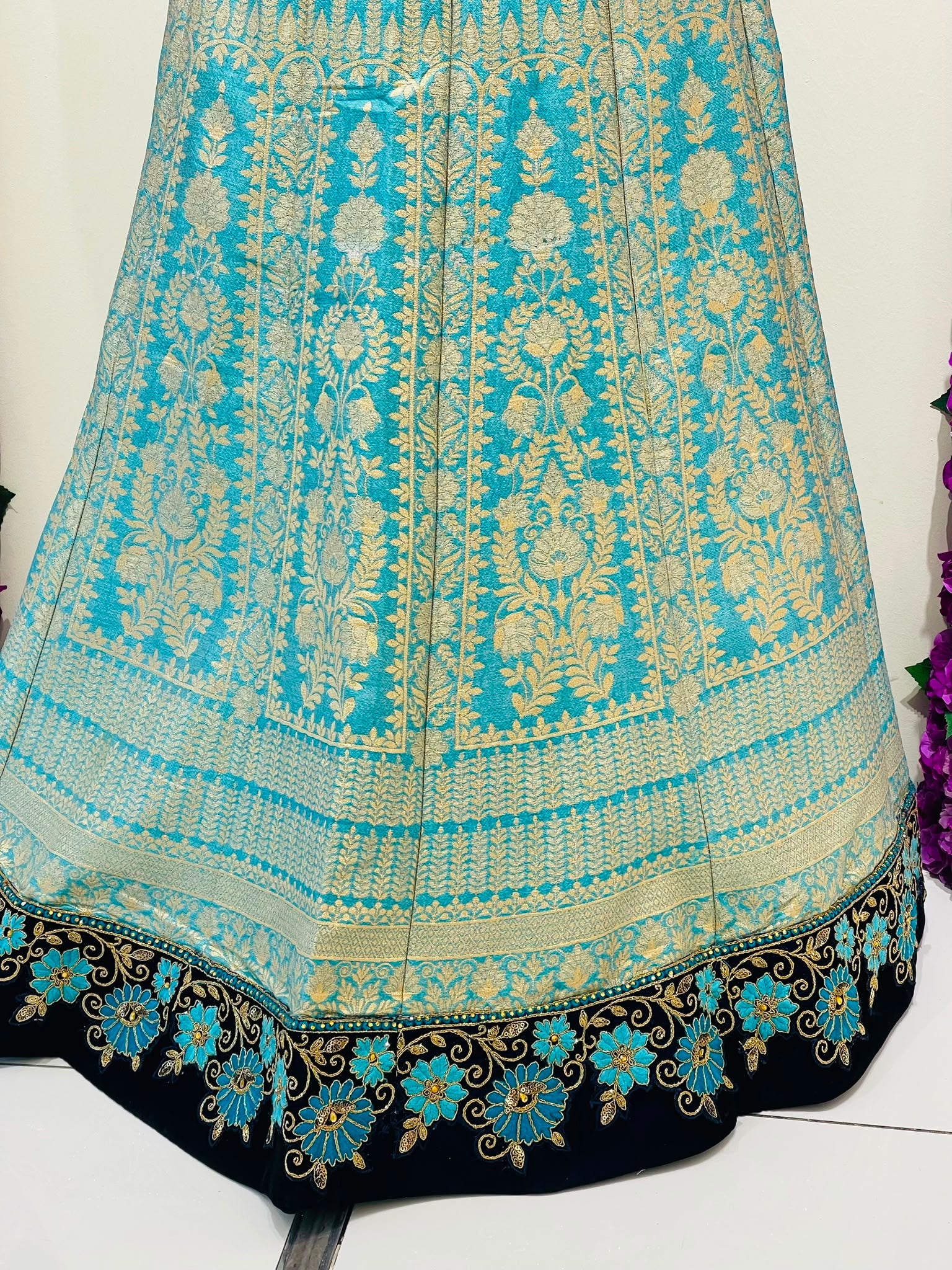 A turquoise blue and gold Banarasi-style embroidered skirt of lehenga with intricate floral motifs and a navy blue border featuring blue and gold floral embroidery 