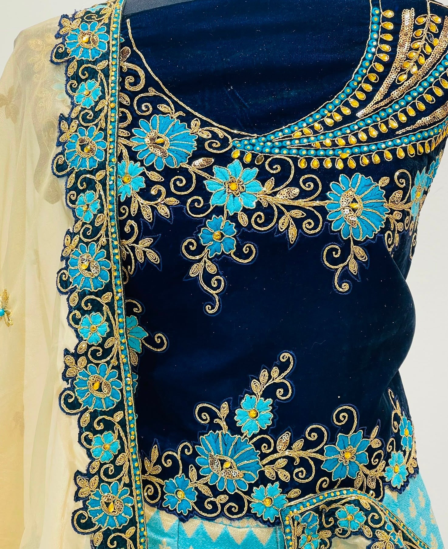 A close-up of a navy blue embroidered blouse with intricate gold and turquoise floral embroidery, paired with a light blue and white patterned bottom and a cream dupatta.