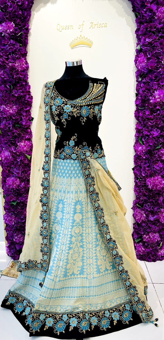A traditional Indian lehenga featuring a navy blue sleeveless blouse with intricate gold and turquoise embroidery, a light blue printed skirt, and a beige dupatta draped over the side.