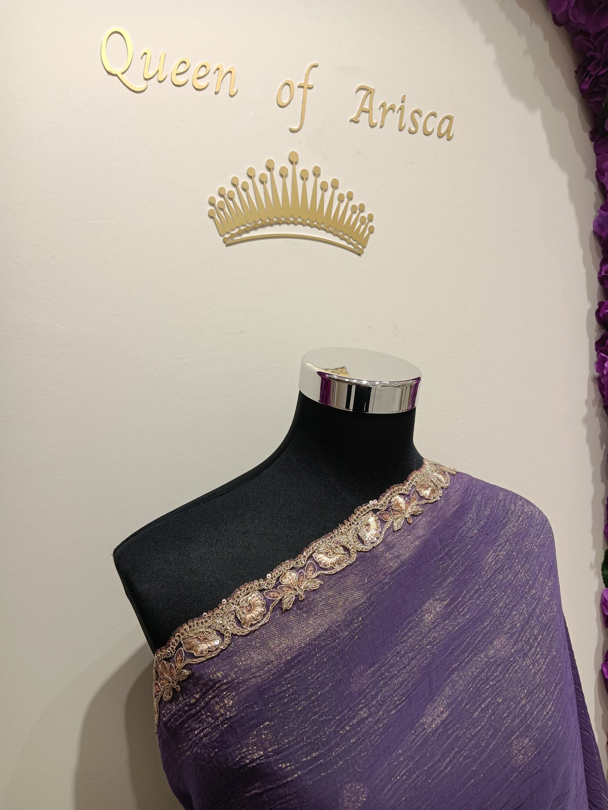 saree features a soft, flowy crushed tissue / shimmer georgette-style fabric with a subtle metallic sheen that catches light beautifully. The color is a rich royal purple (deep violet), giving it a regal and evening-ready appeal. 