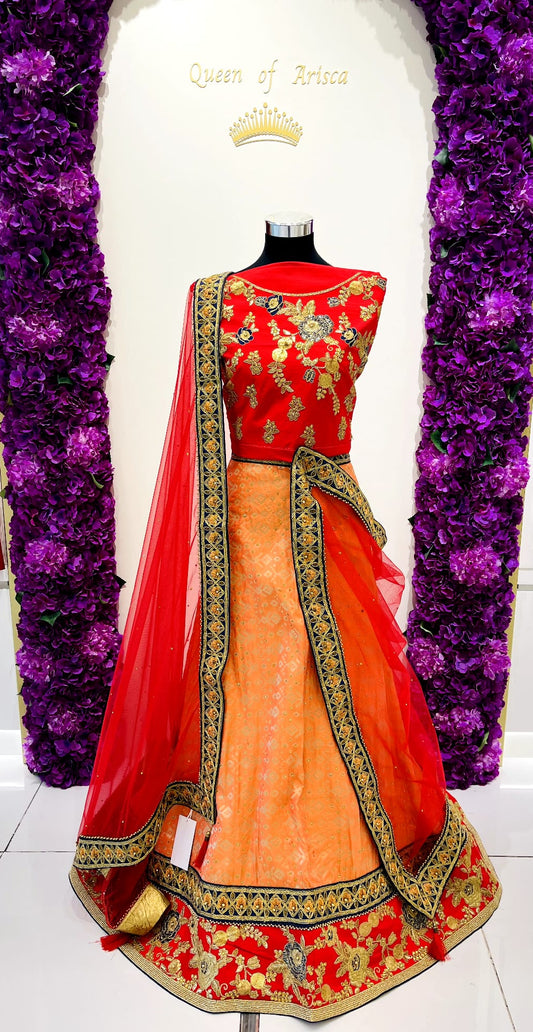 A traditional Indian lehenga . The outfit features a bright red sleeveless embroidered bodice, a peach-orange flared skirt, and a red dupatta with gold and navy blu borders. 