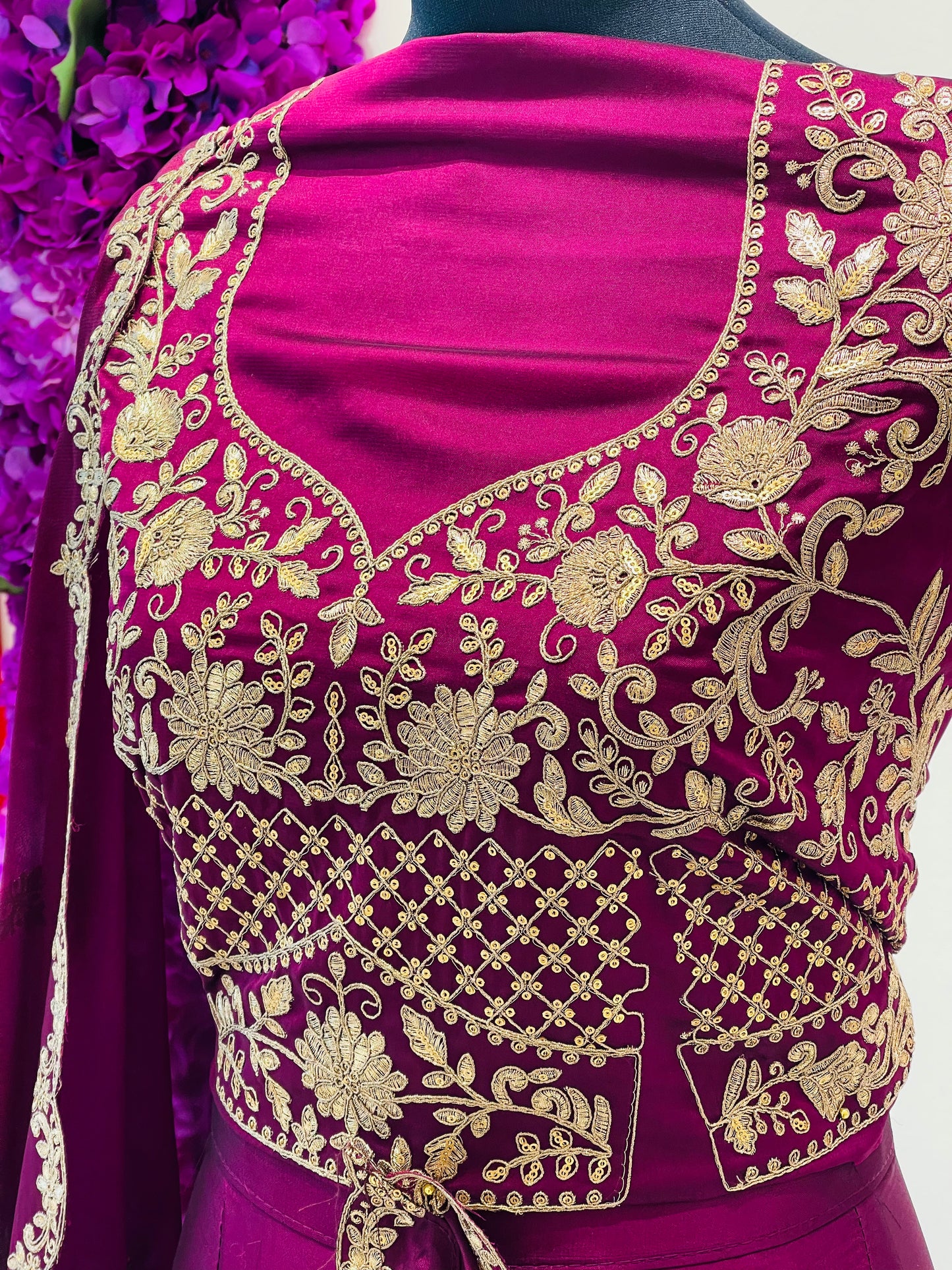 A close-up of a magenta velvet blouse with intricate gold floral embroidery and mirror work.