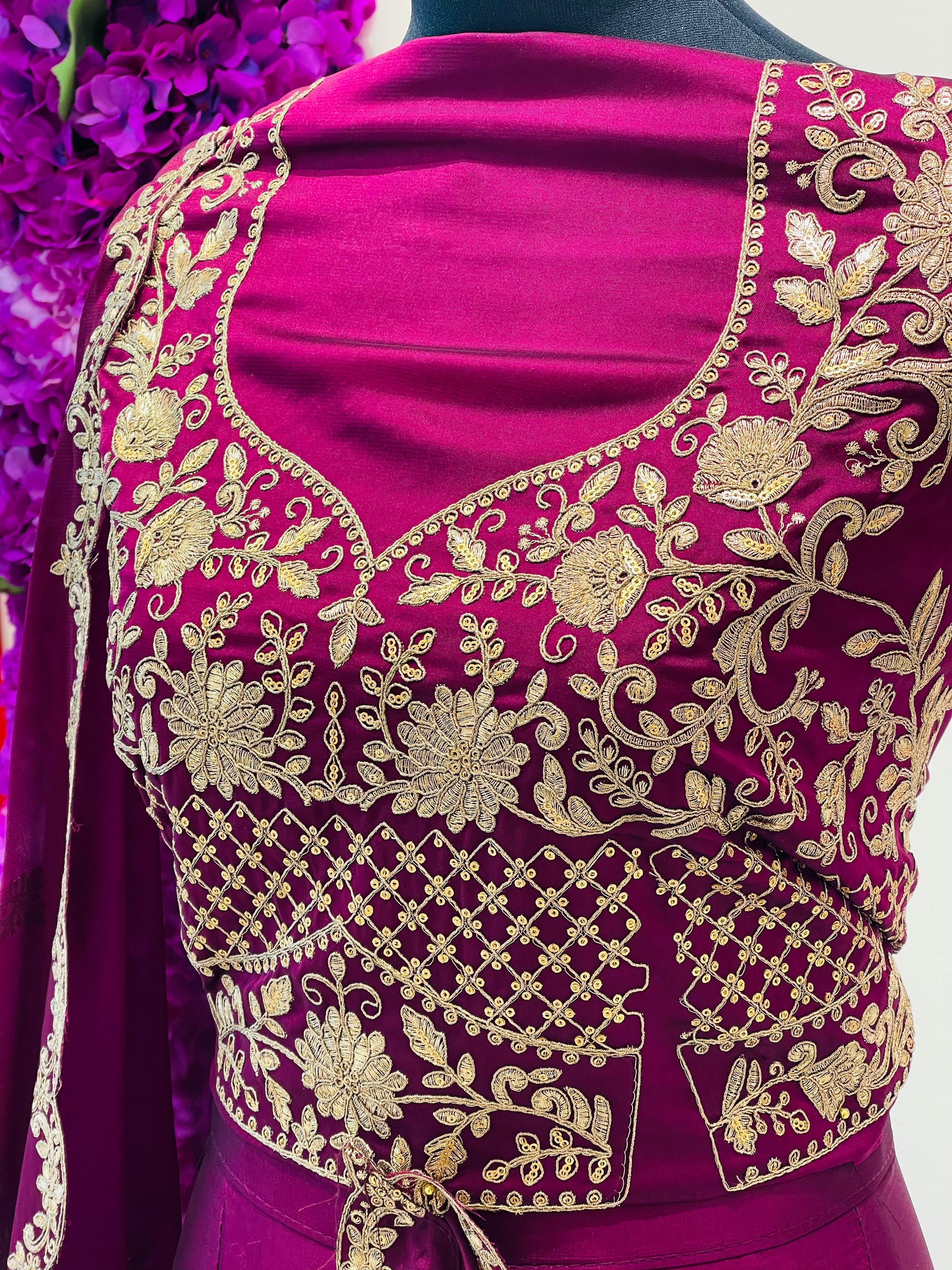 A close-up of a magenta velvet blouse with intricate gold floral embroidery and mirror work.
