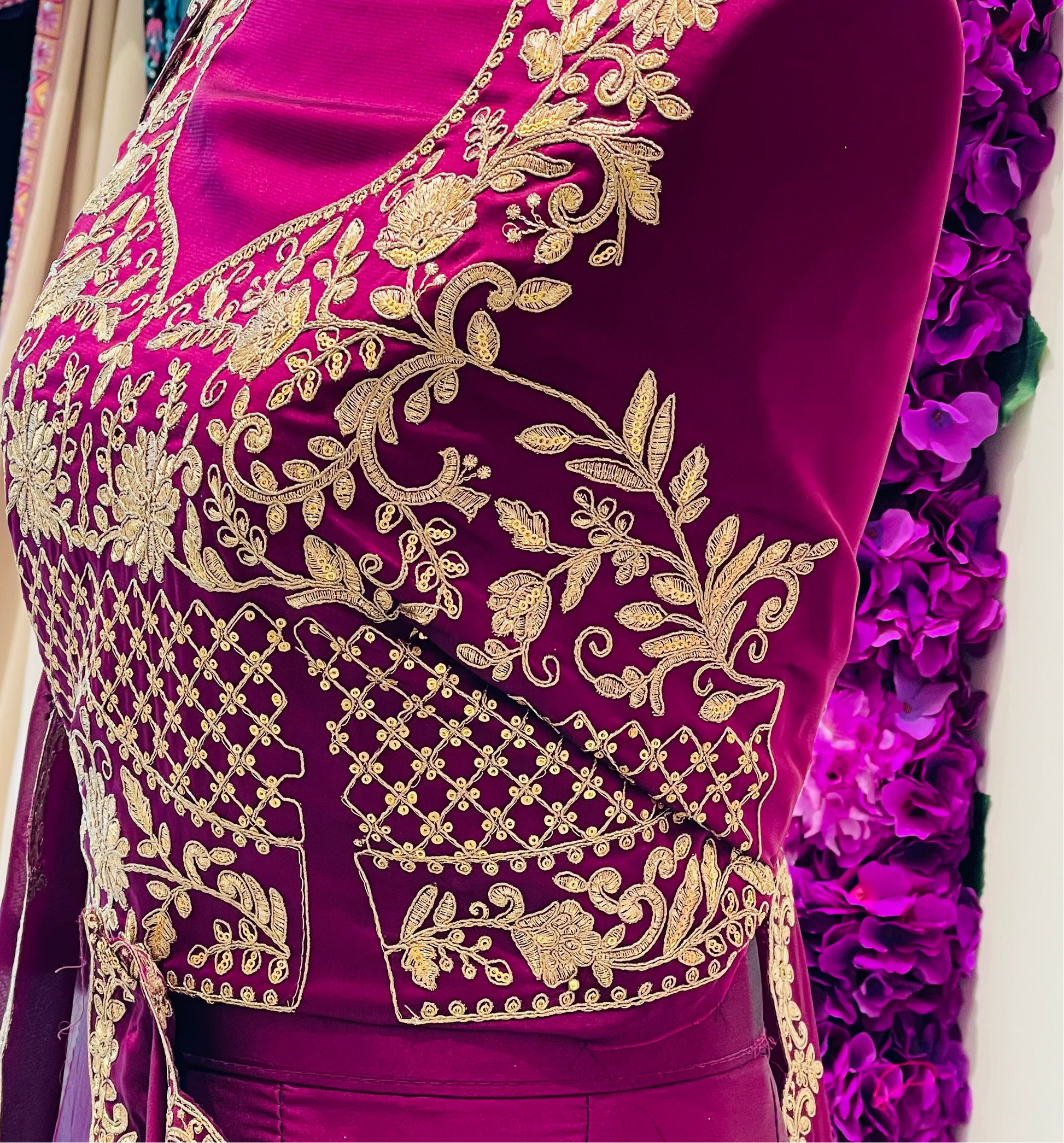 A close-up of a magenta purple traditional outfit blouse with intricate gold embroidery on the bodice and border details.