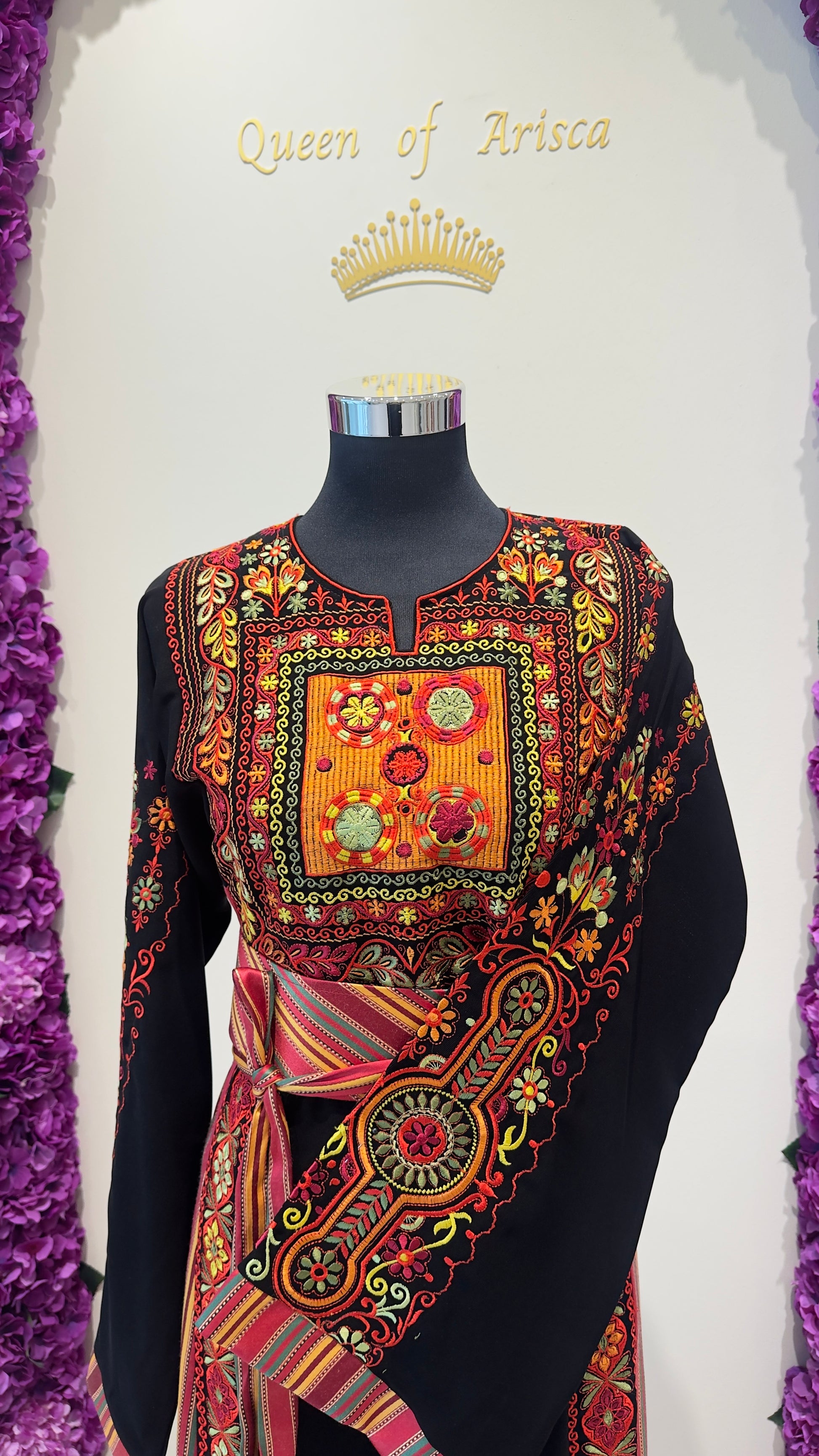 Colorful embroidered top on a mannequin with 'Queen of Artisa' branding.