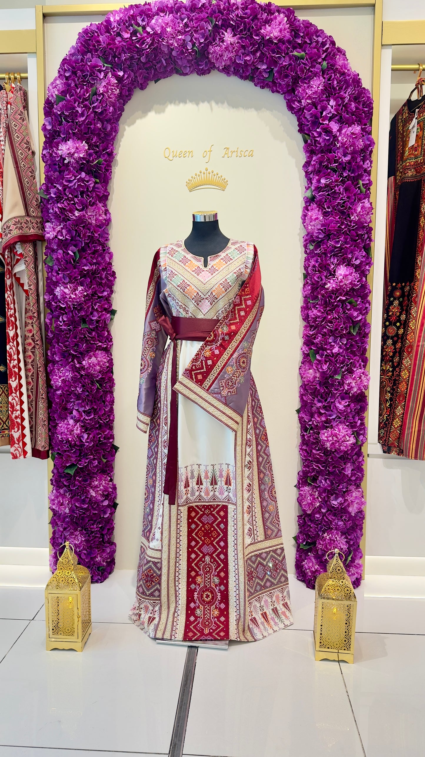 Thobe displayed on a mannequin with a purple floral arch and gold lanterns in a store setting.