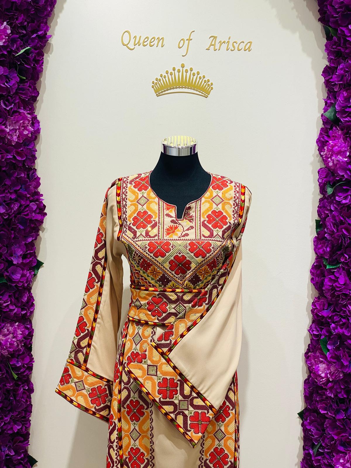 Champagne beige Palestinian-inspired thobe with red and orange geometric embroidery at Arisca Qatar.