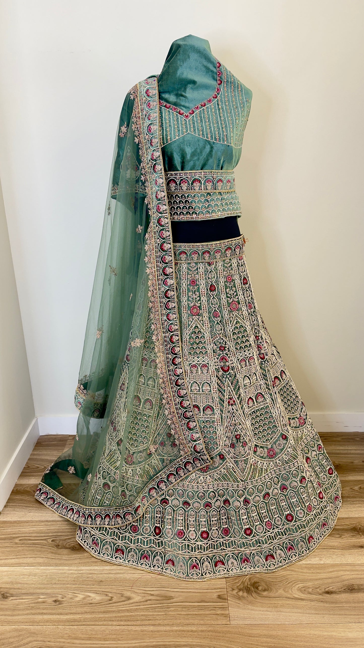 Traditional green embroidered lehenga with matching blouse on a wooden floor.