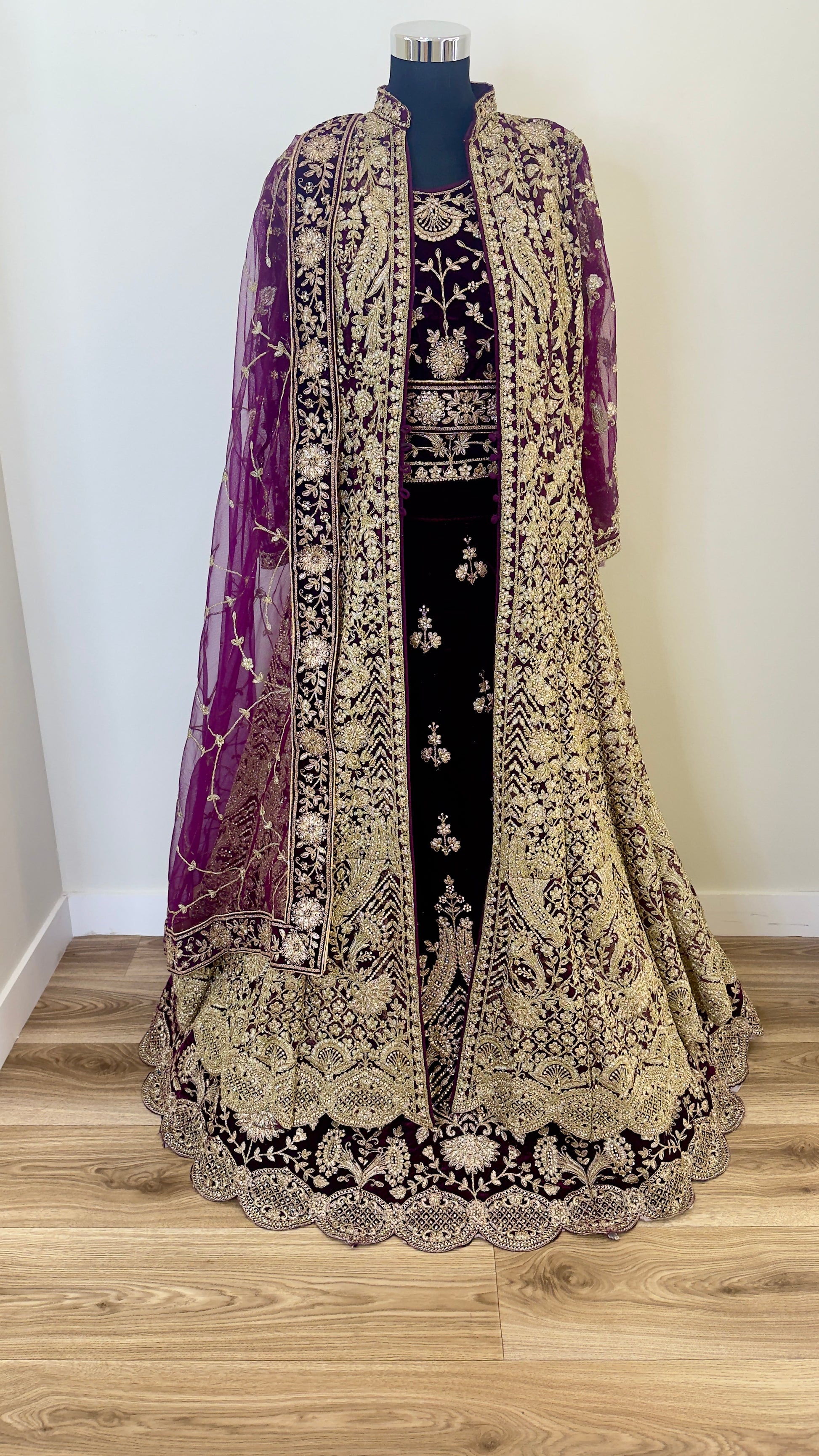 Traditional embroidered outfit with a purple dupatta on a wooden floor.