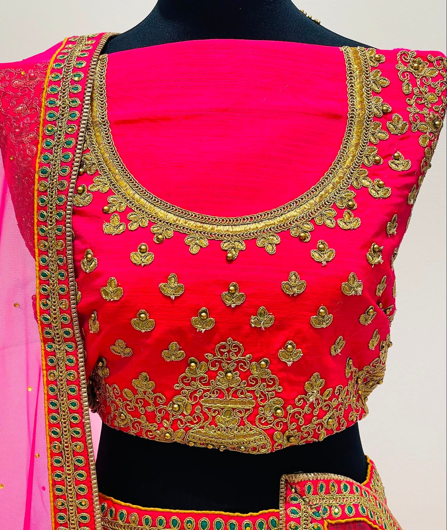 A bright pink embroidered blouse with gold metallic detailing and a matching pink dupatta draped over the shoulders.