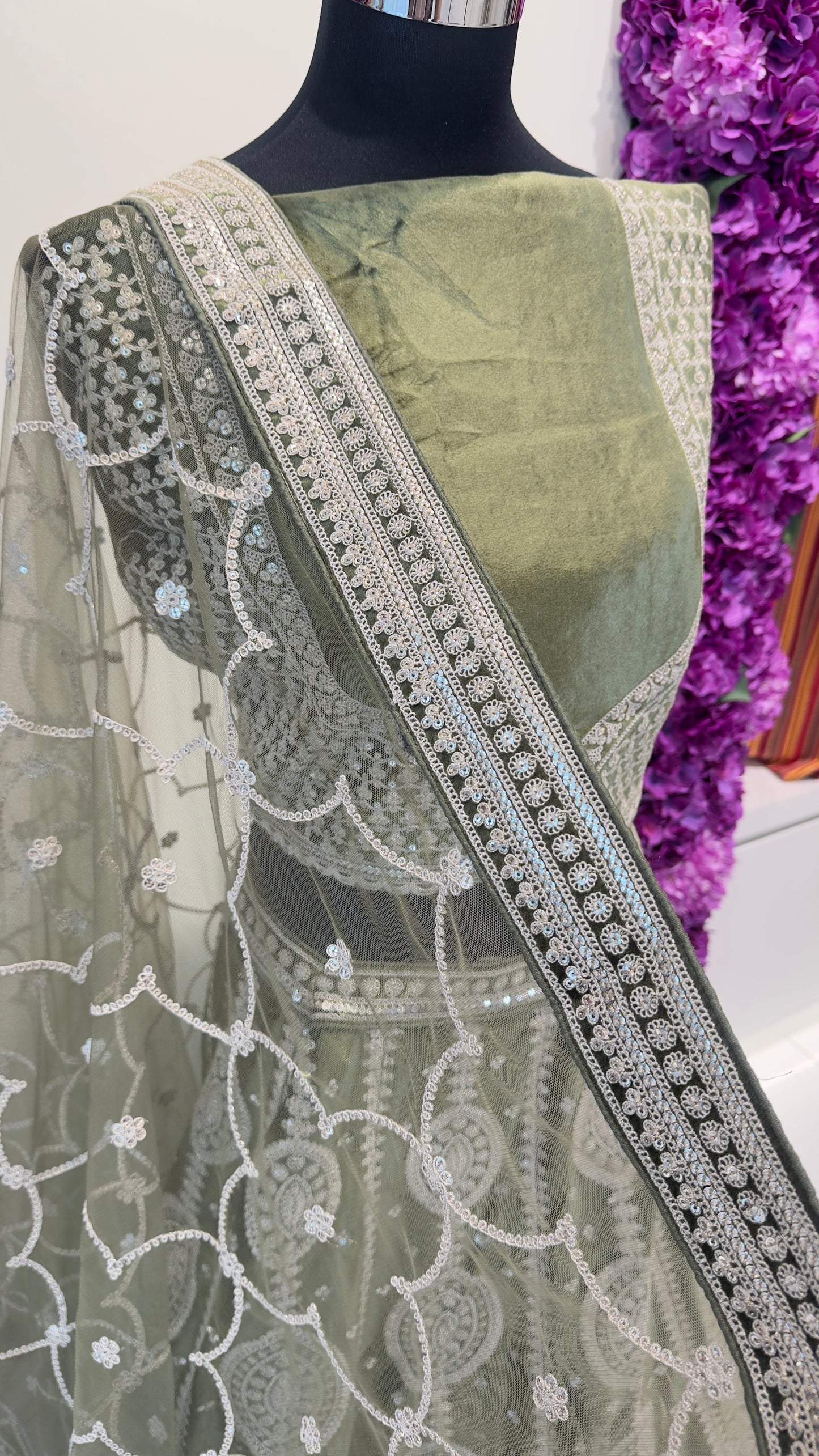 Green saree with intricate white embroidery on a mannequin against a purple floral background