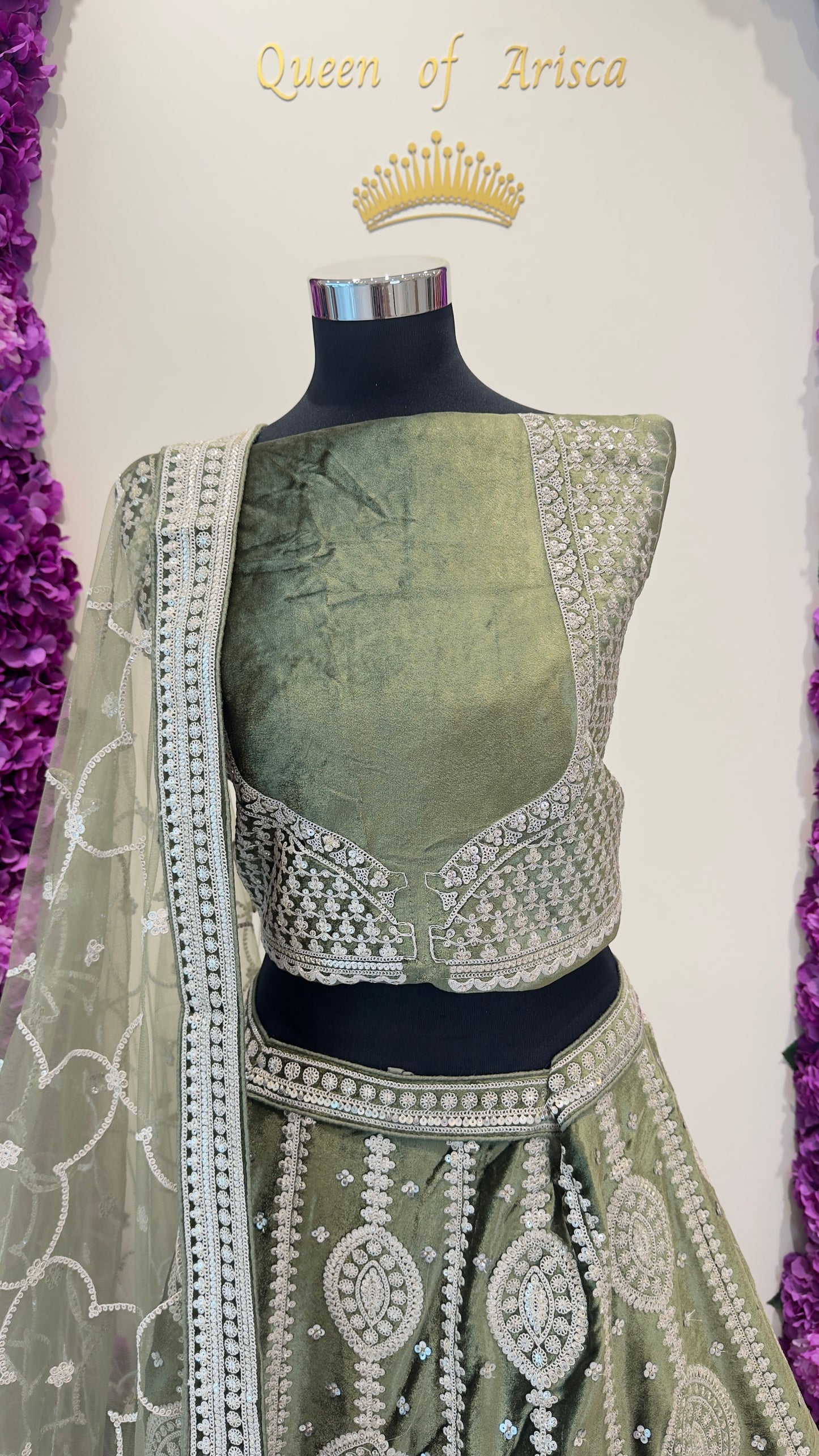 Green embroidered lehenga with silver detailing on a mannequin against a white background.