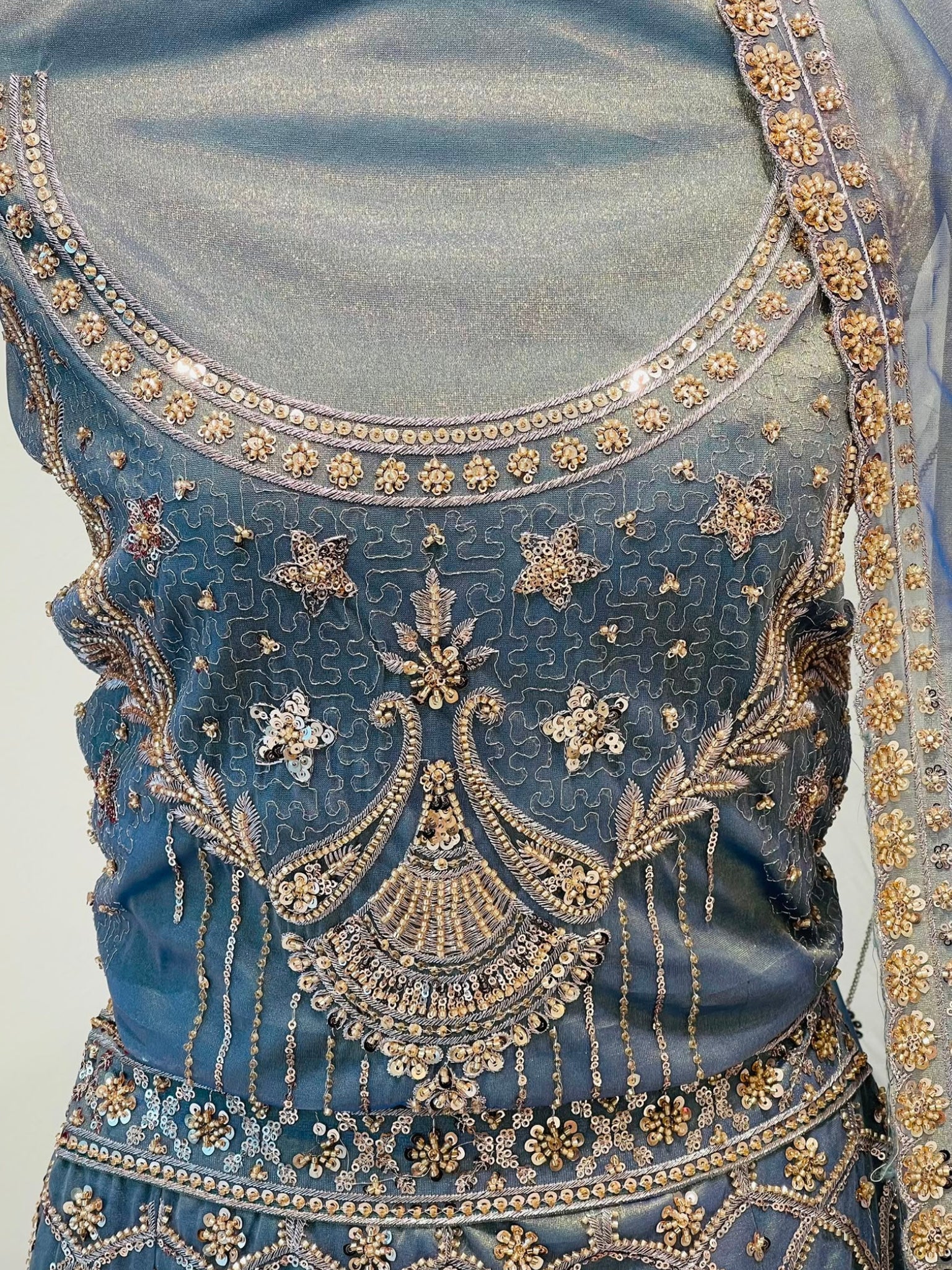A close-up of a blue traditional embroidered , featuring intricate metallic gold and silver beadwork, sequins, and embroidery around the neckline, bodice, and lower hem.