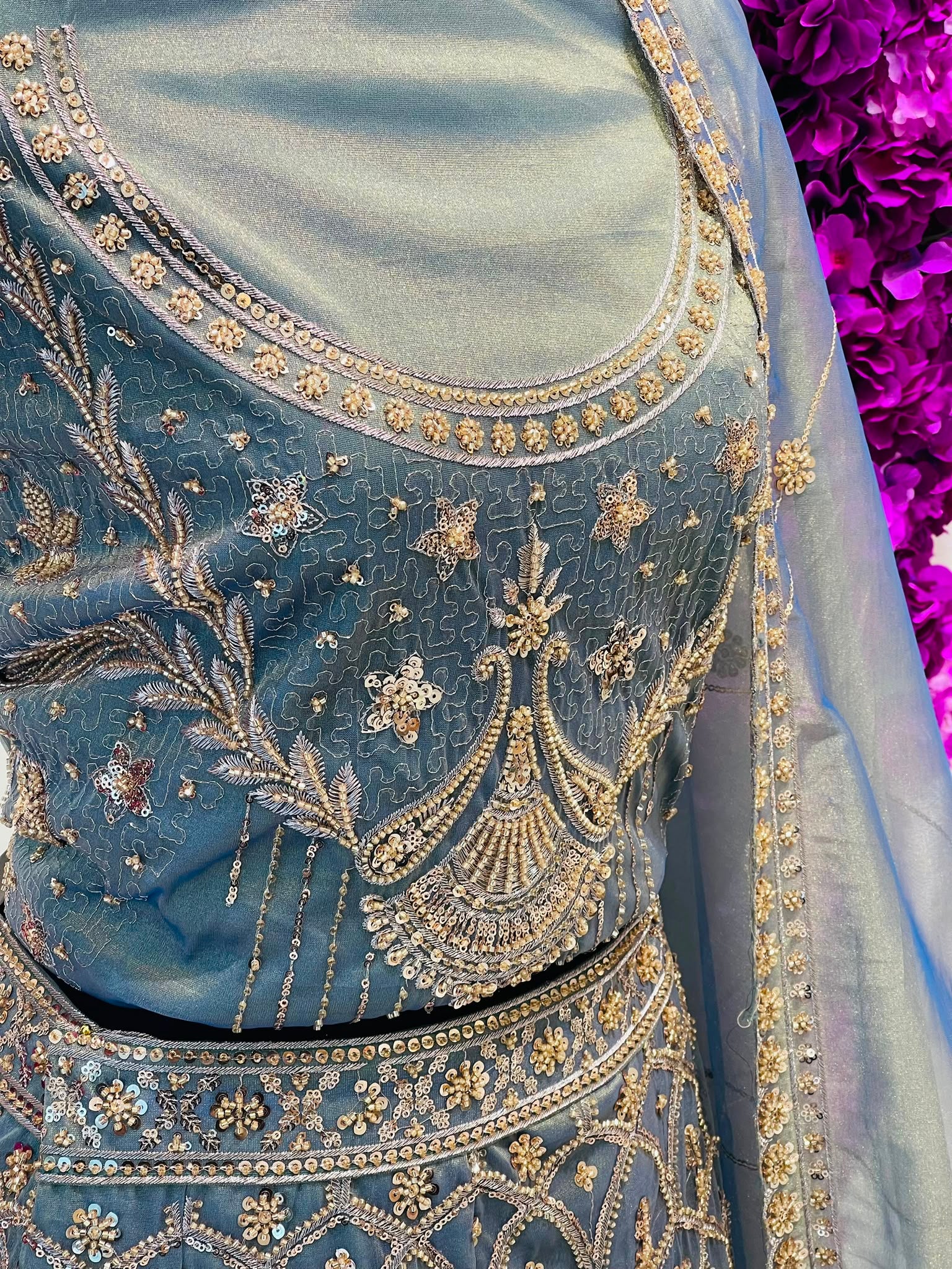 A close-up of a light blue embroidered traditional outfit with intricate gold and silver beadwork, floral patterns, and a matching sheer dupatta draped over the shoulder.